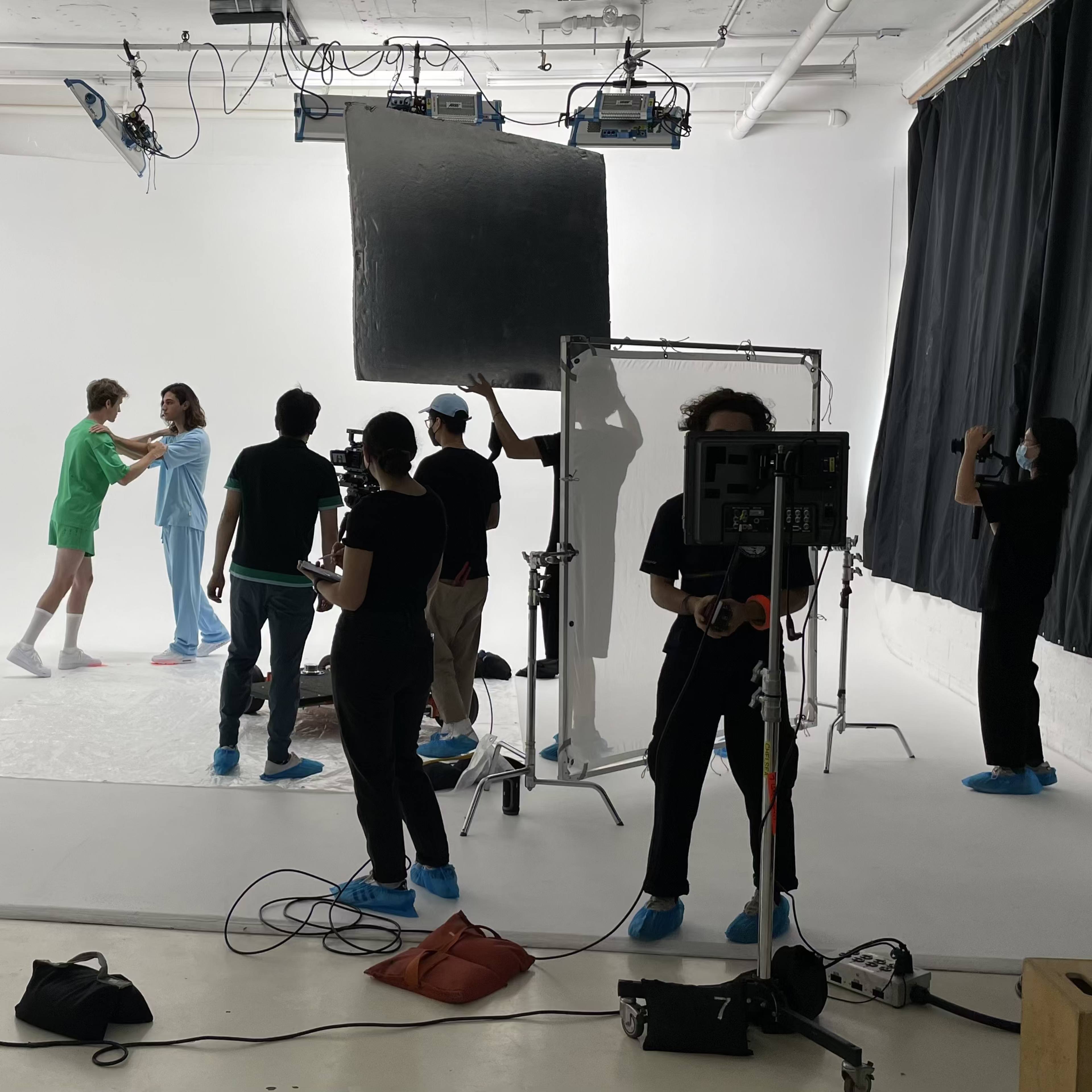 A photography studio scene shows a photoshoot with models and a crew set up against a white backdrop.