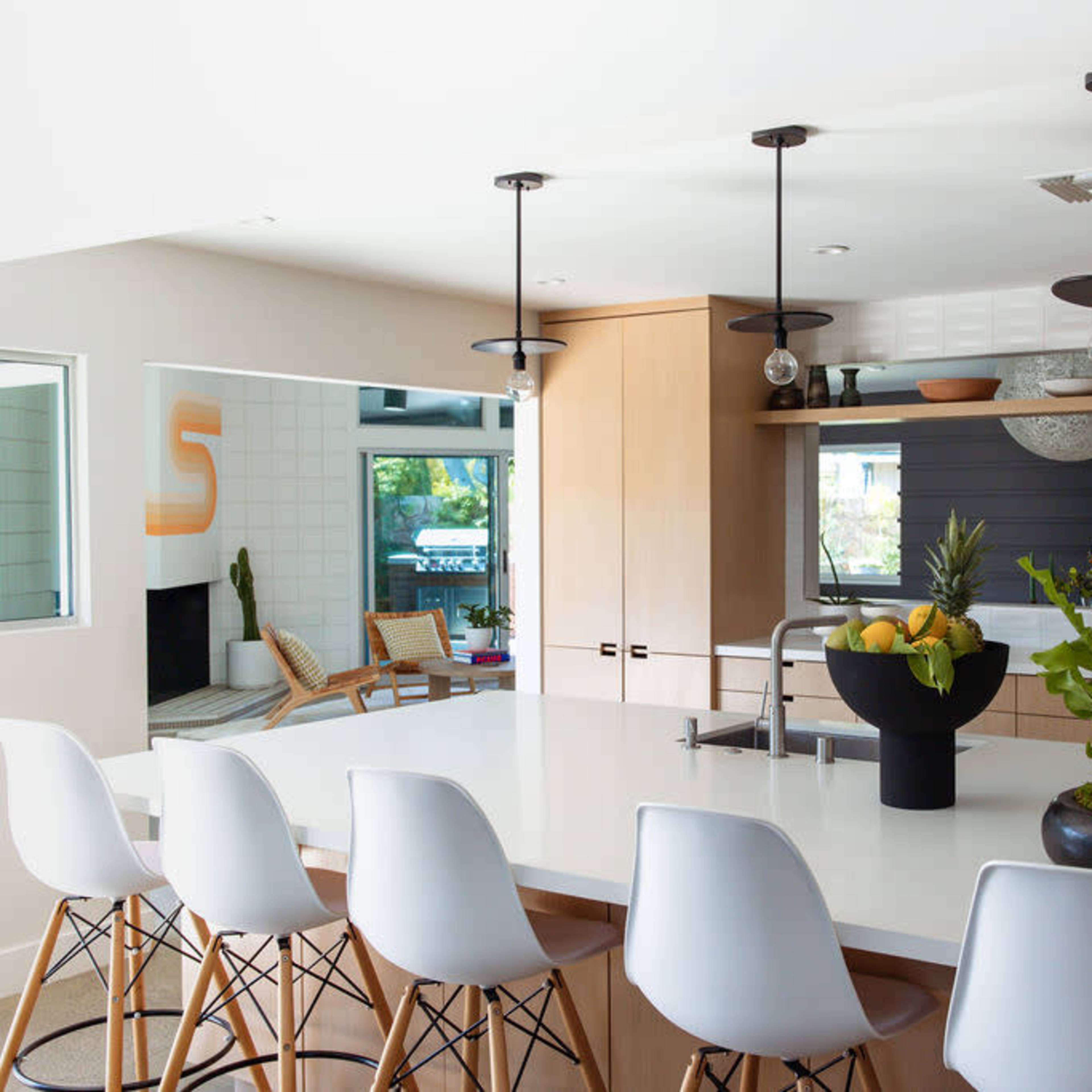 A modern kitchen features a large white island with stools, surrounded by wooden cabinetry and large windows.