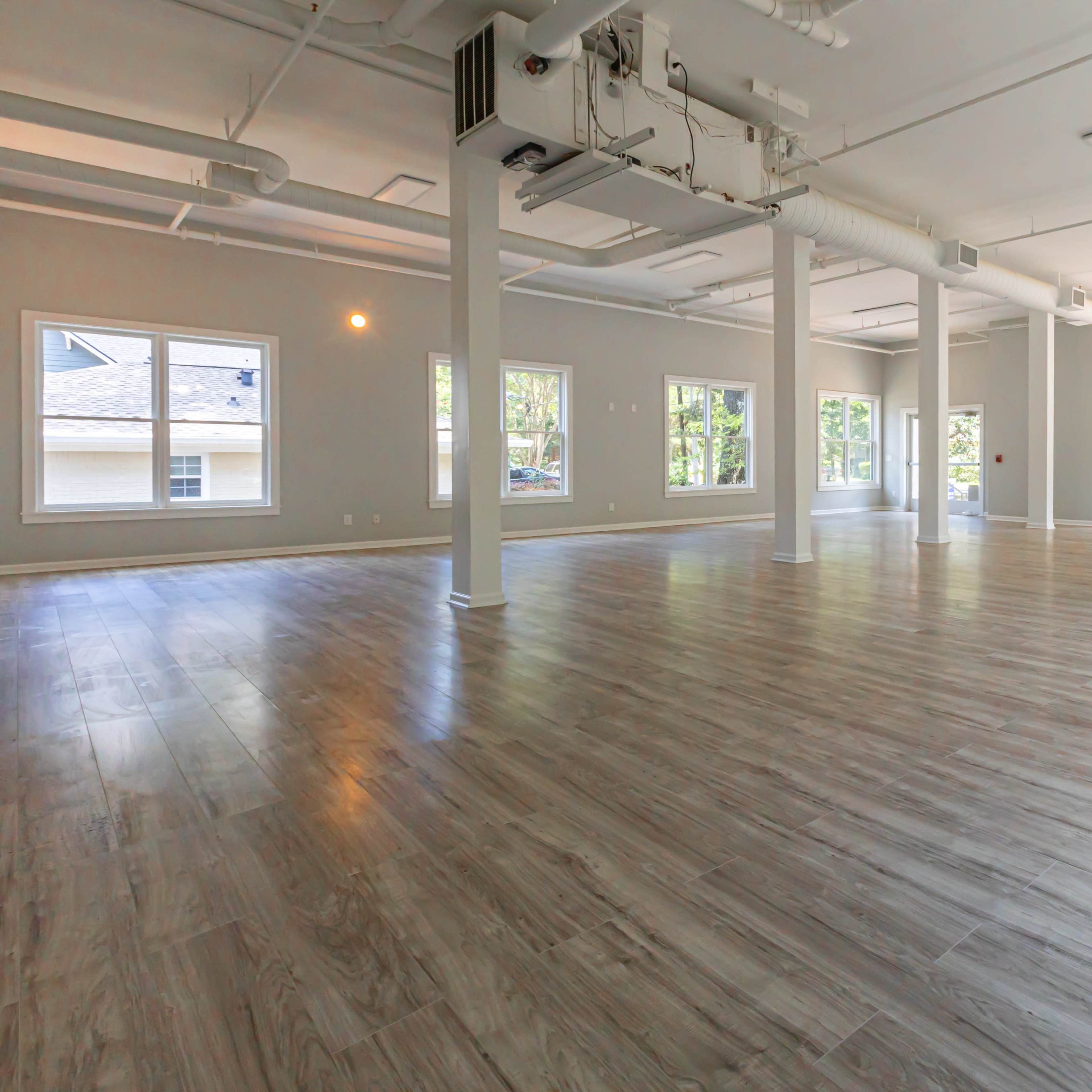 A spacious, empty room with large windows and wooden flooring.