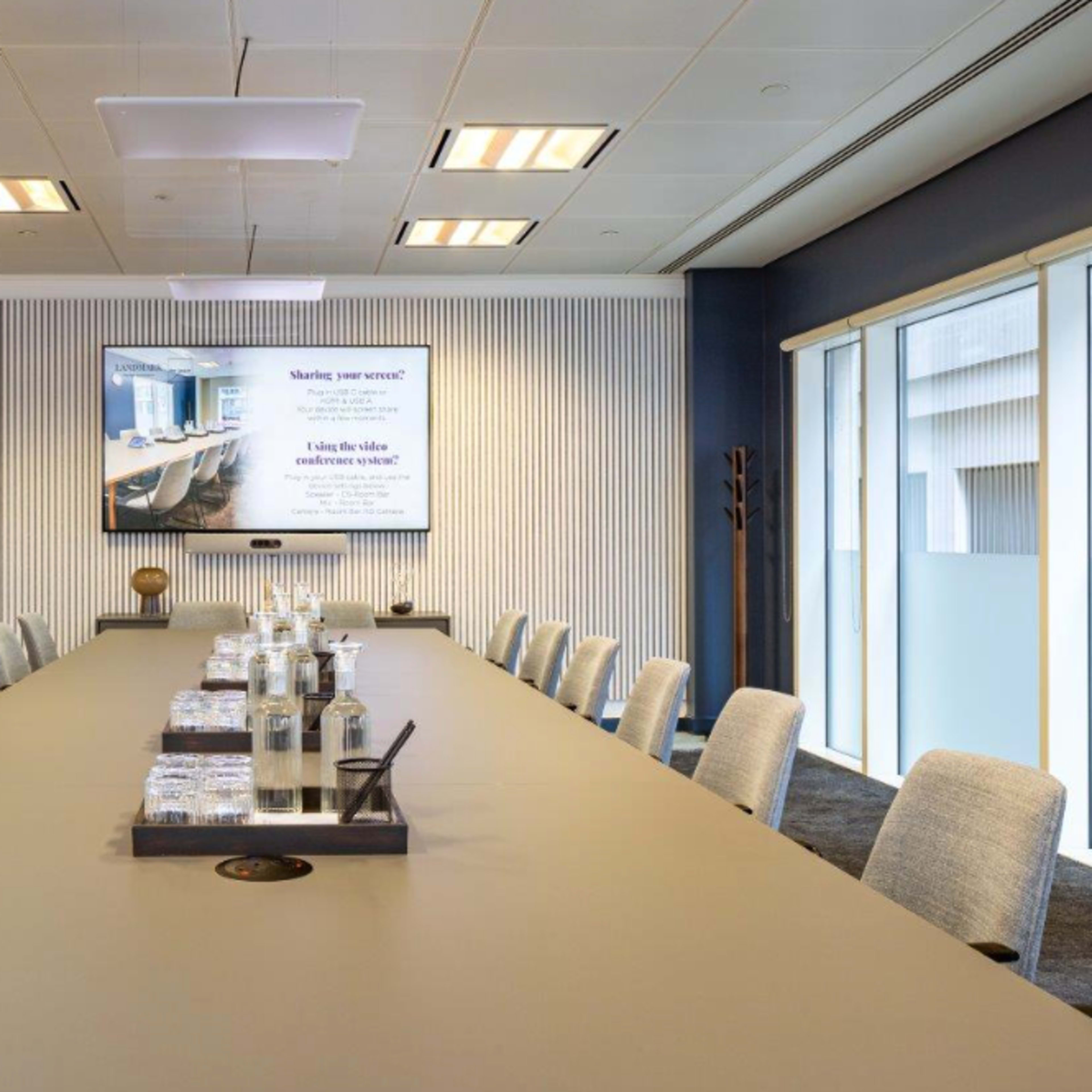 A modern conference room features a long table set with water bottles and glasses, along with a large screen displaying a presentation.