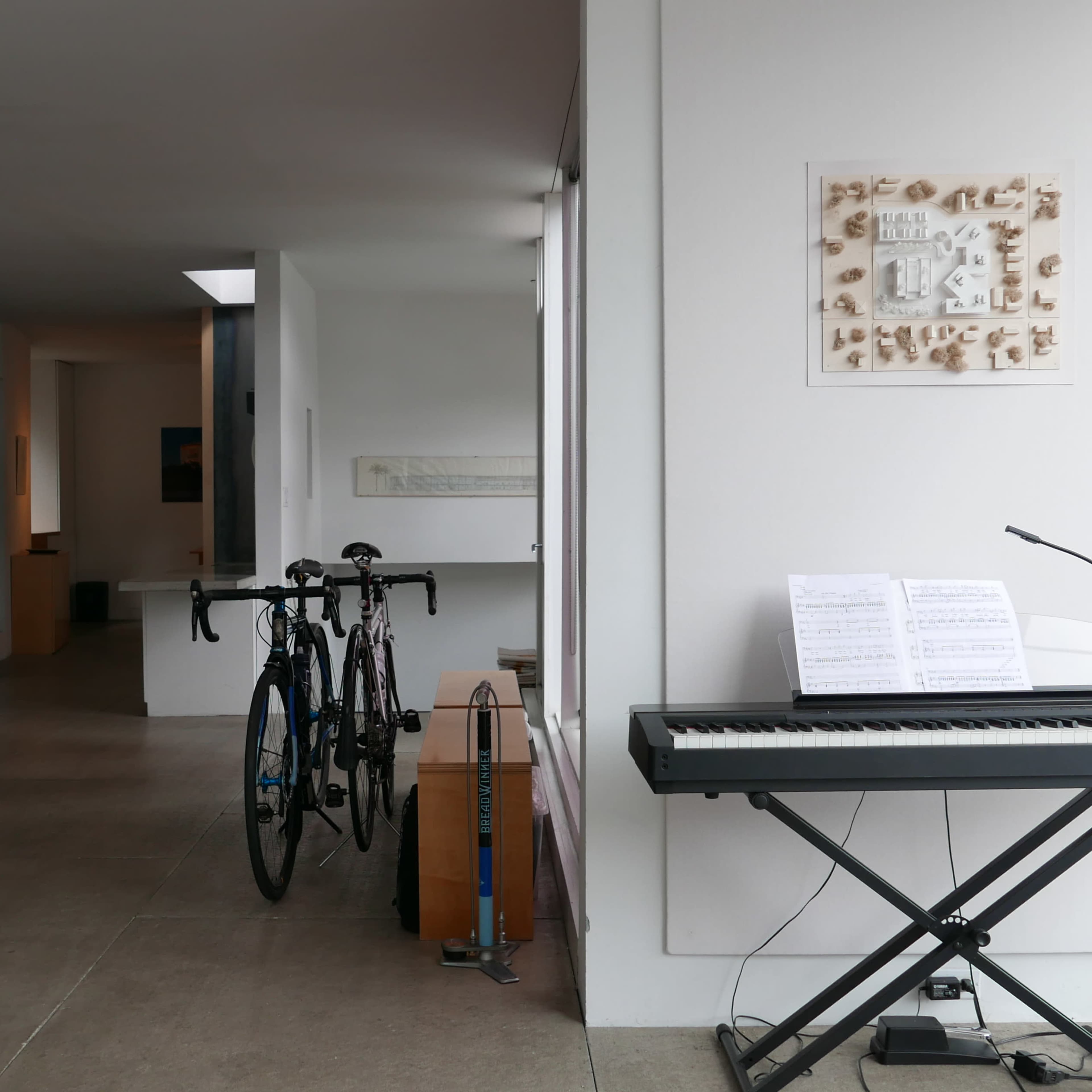 A modern interior space featuring bicycles parked near a keyboard and sheet music, with an open layout that includes a workspace and art on the walls.