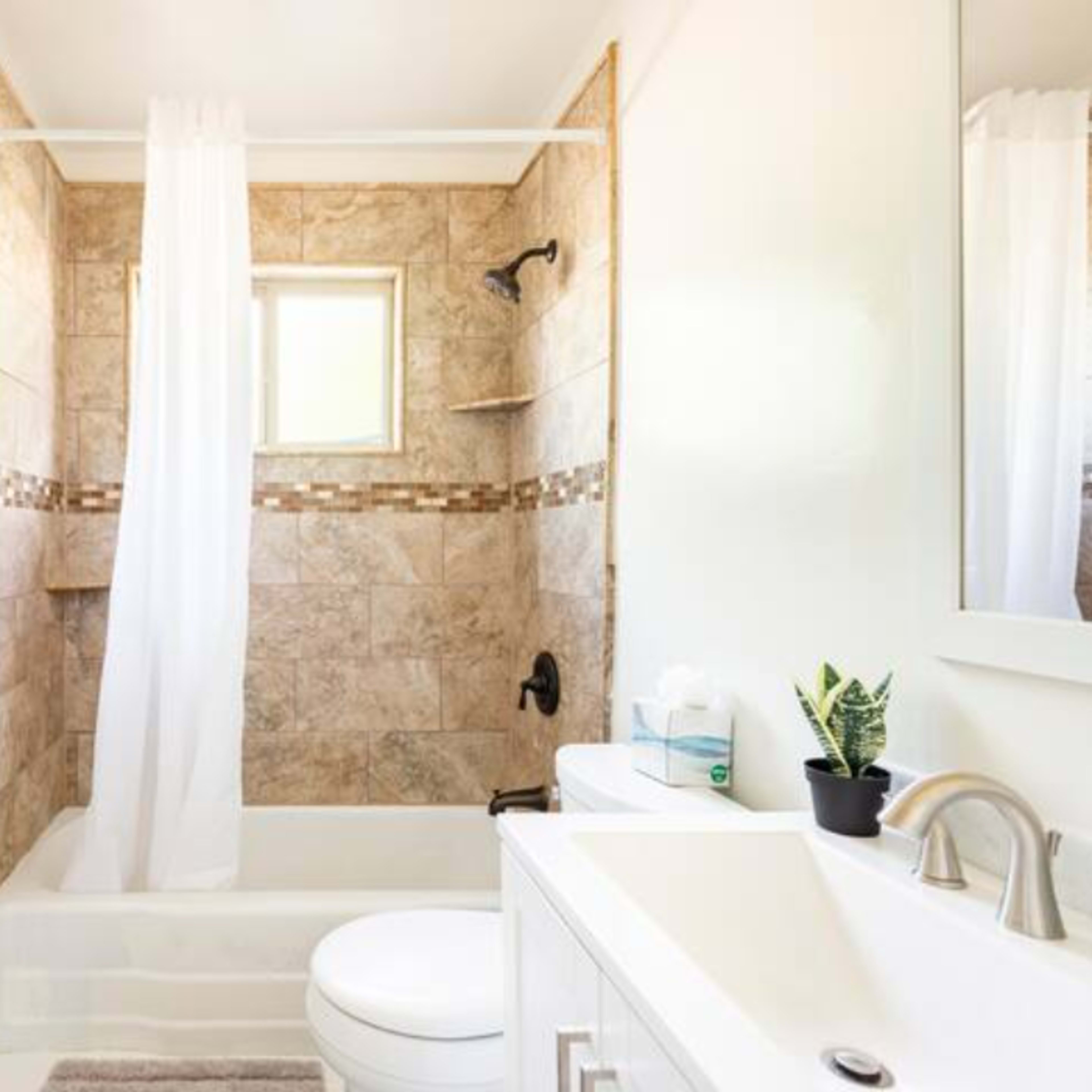 A compact bathroom featuring a bathtub with a shower curtain, a toilet, a small vanity with a mirror, and stone-patterned walls.