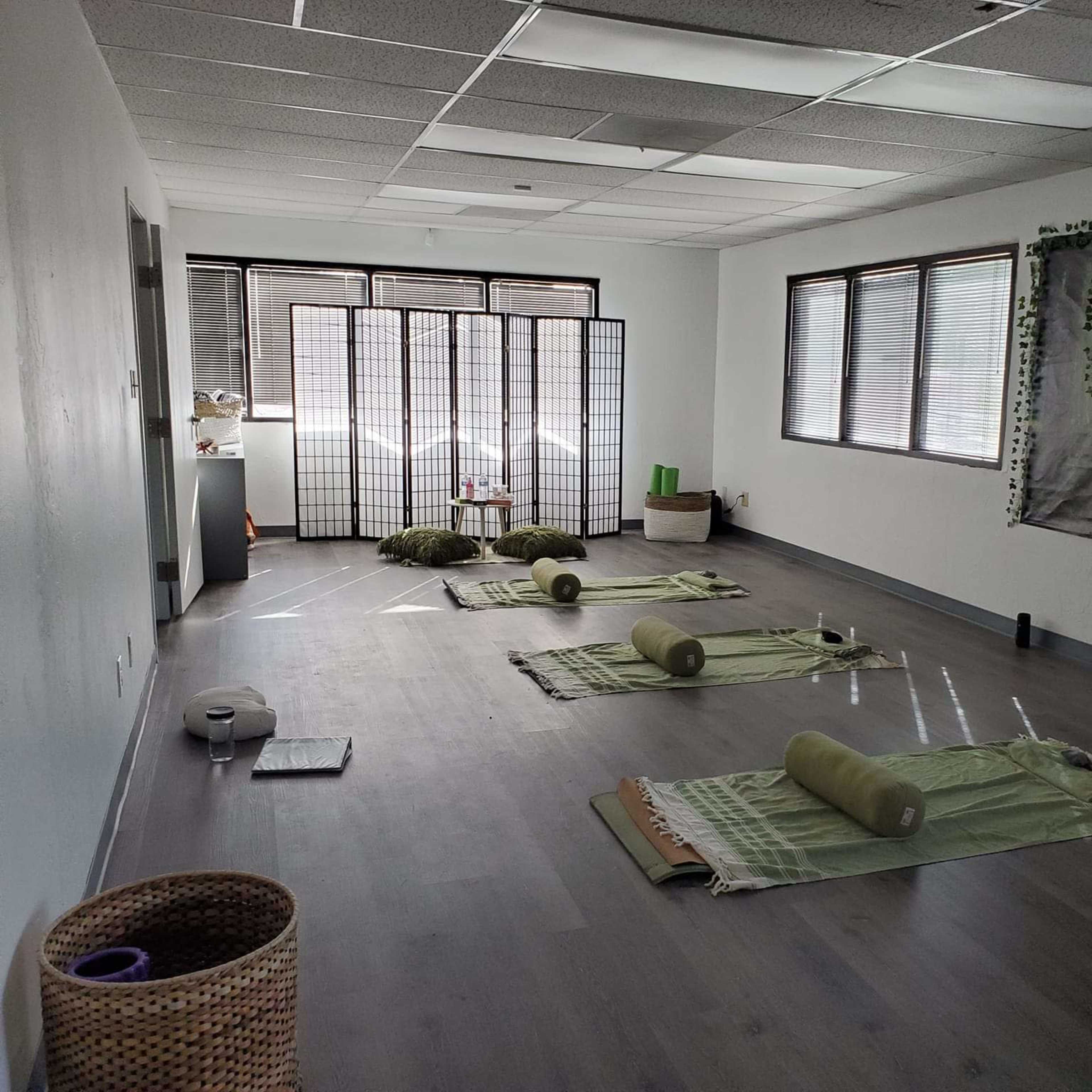 A sparsely furnished yoga or meditation studio with mats laid out on the floor and folding screens in the background.