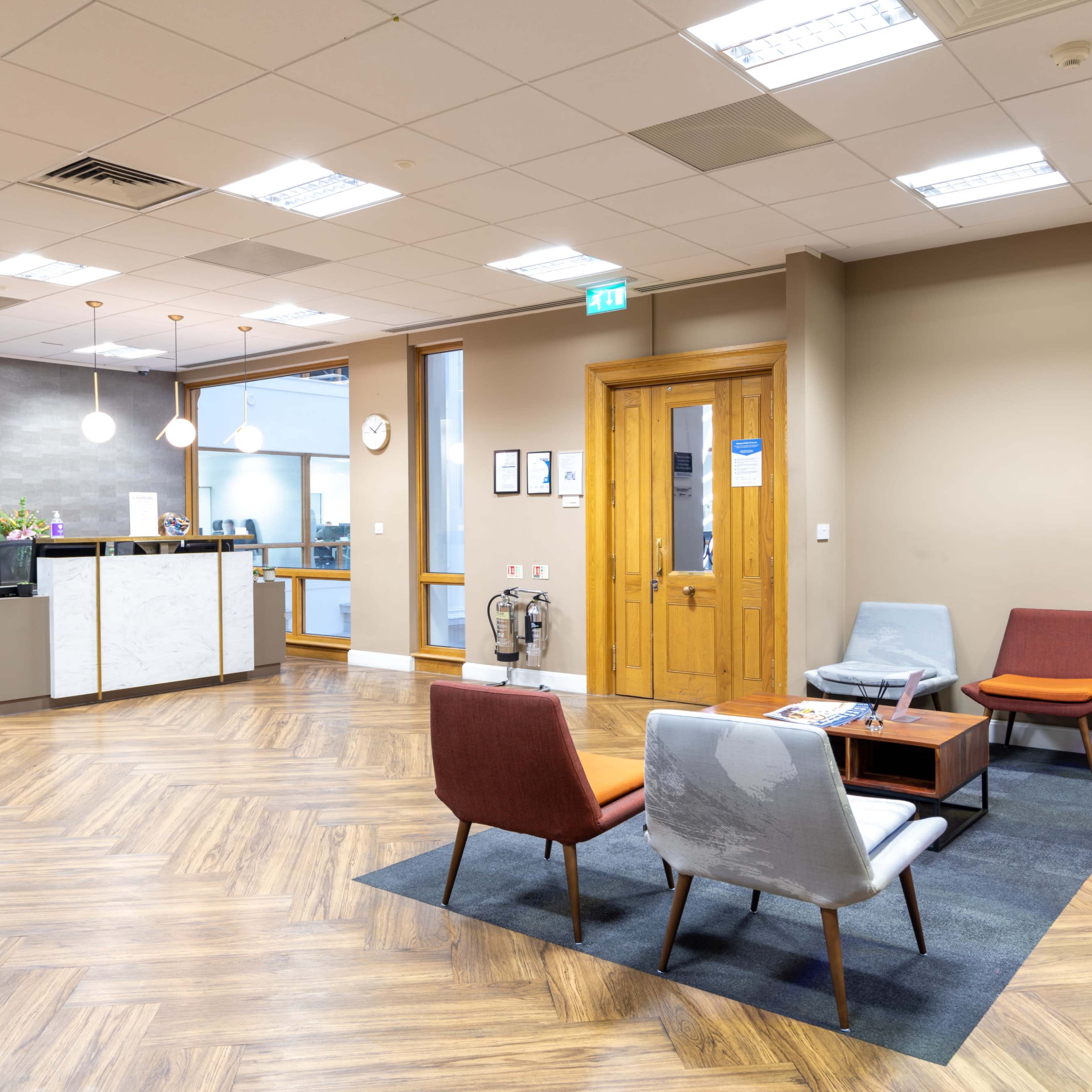 A modern office reception area with a seating arrangement, a reception desk, and wooden flooring.