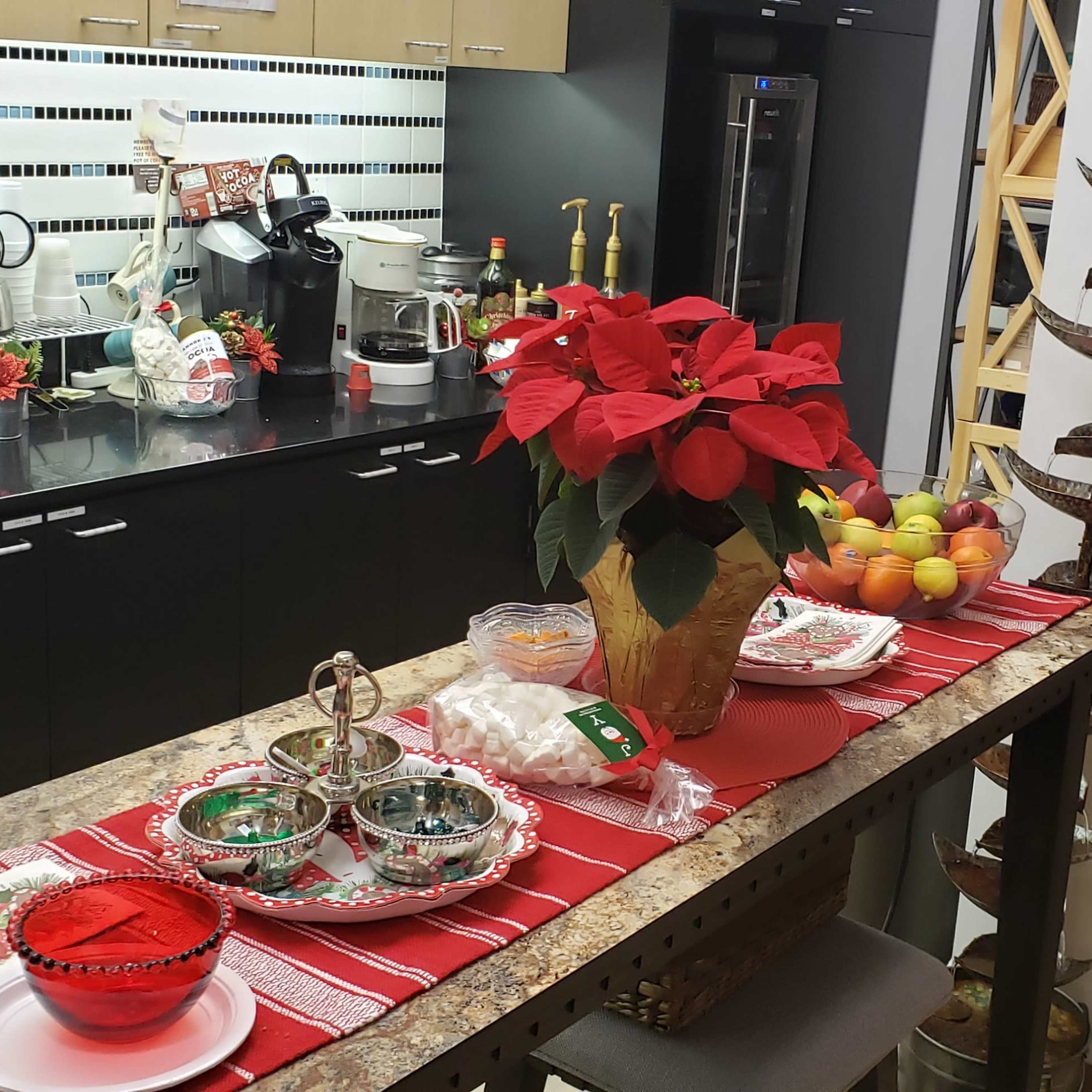 A kitchen area is decorated with holiday items, featuring a countertop with poinsettias, snacks, and colorful dishes against a backdrop of modern appliances.