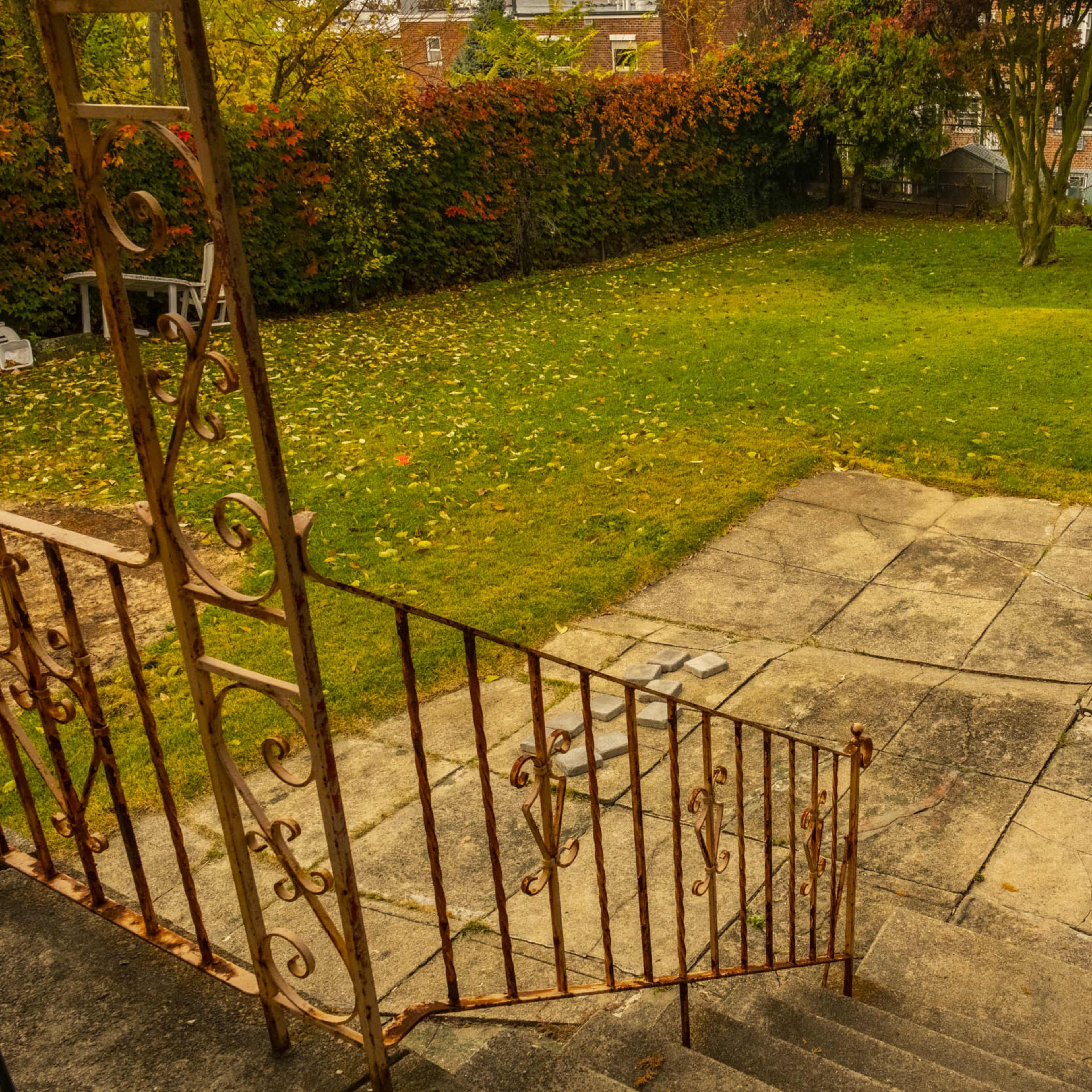 A staircase with ornate railings leading down to a grassy yard surrounded by shrubs and trees.
