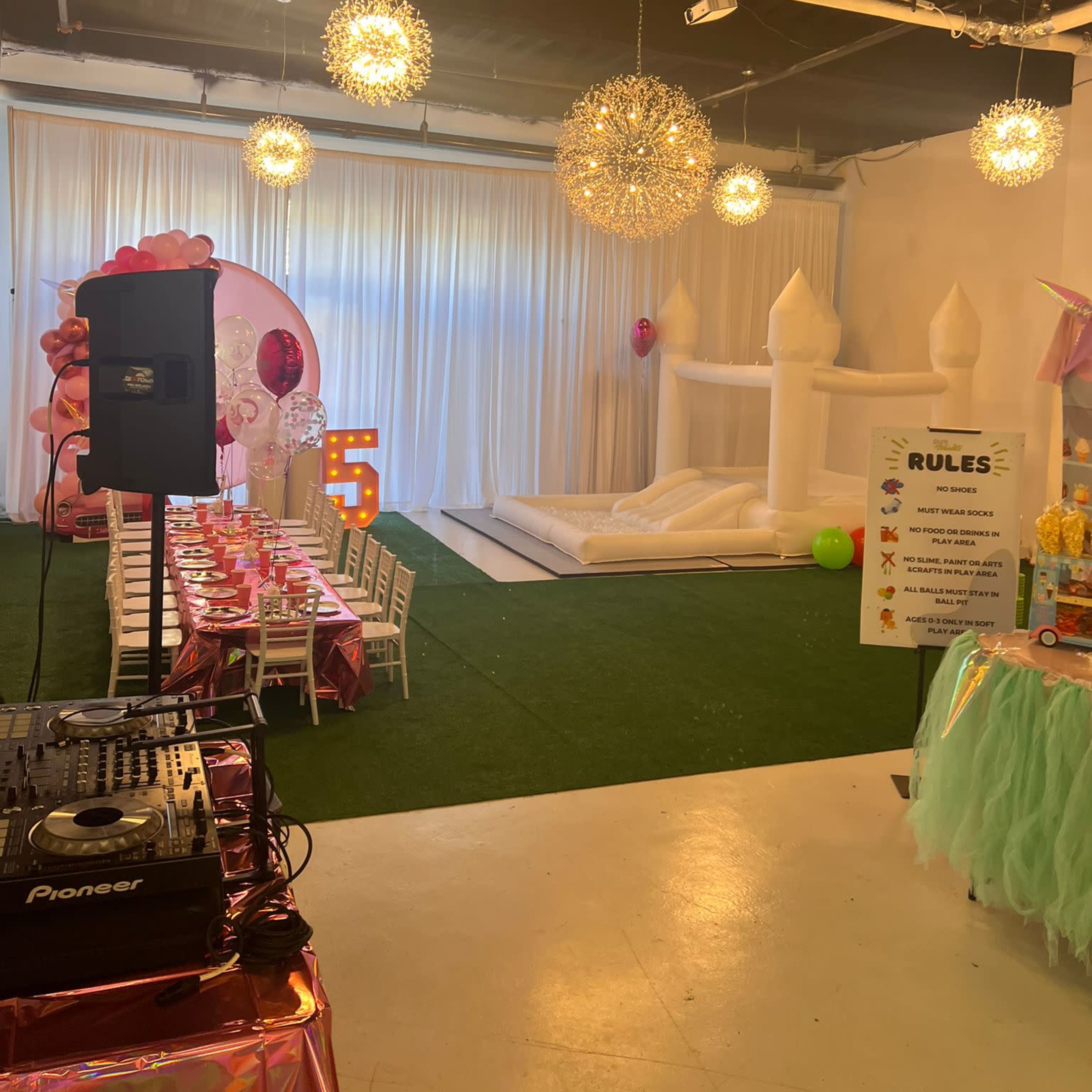 An indoor party scene featuring a decorated table, a bouncy castle, and festive lighting.