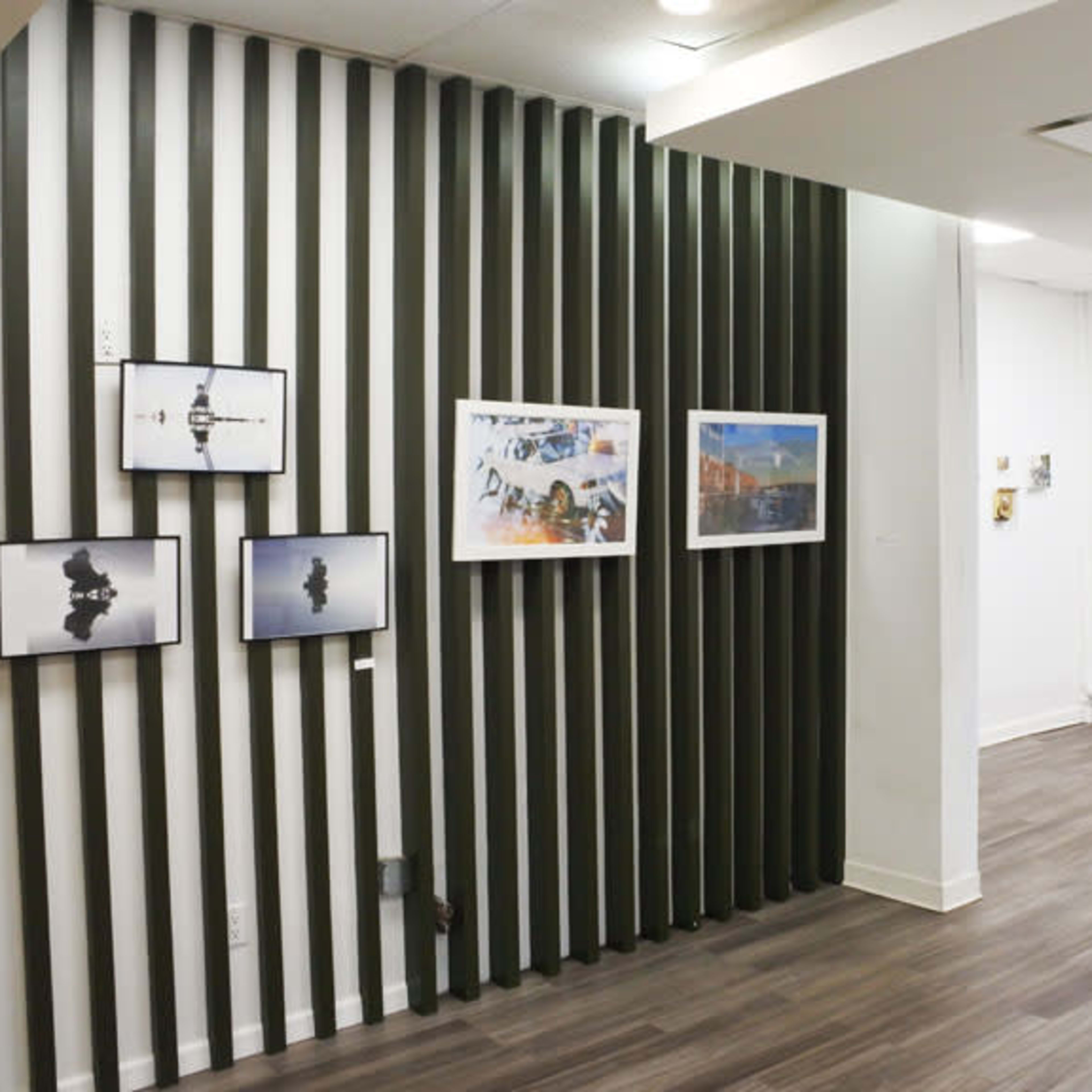 An art gallery with framed photographs and artwork displayed on the walls, featuring a green and white striped column in the background.