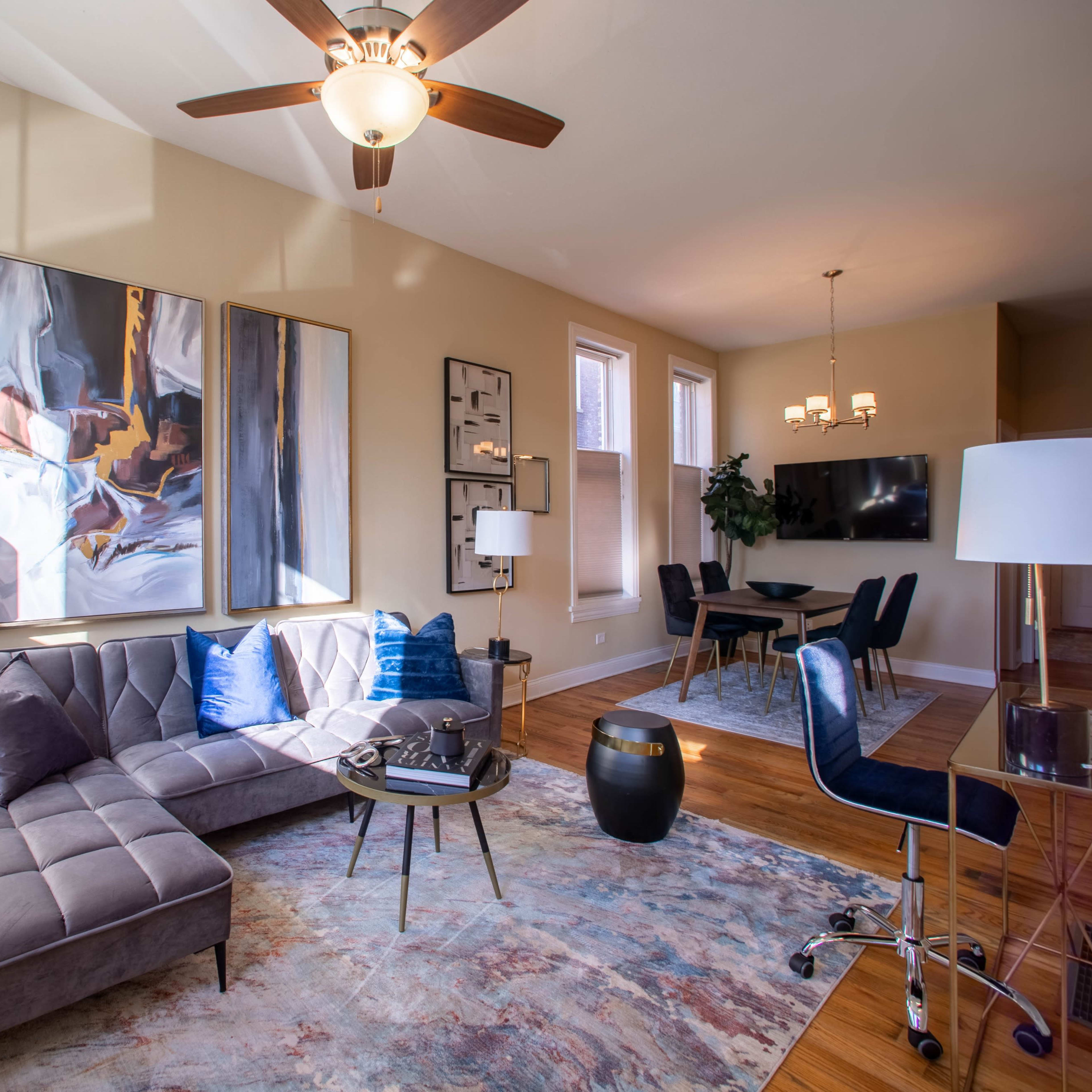 A modern living room with a sectional sofa, a circular coffee table, an artwork on the wall, and a dining area in the background.