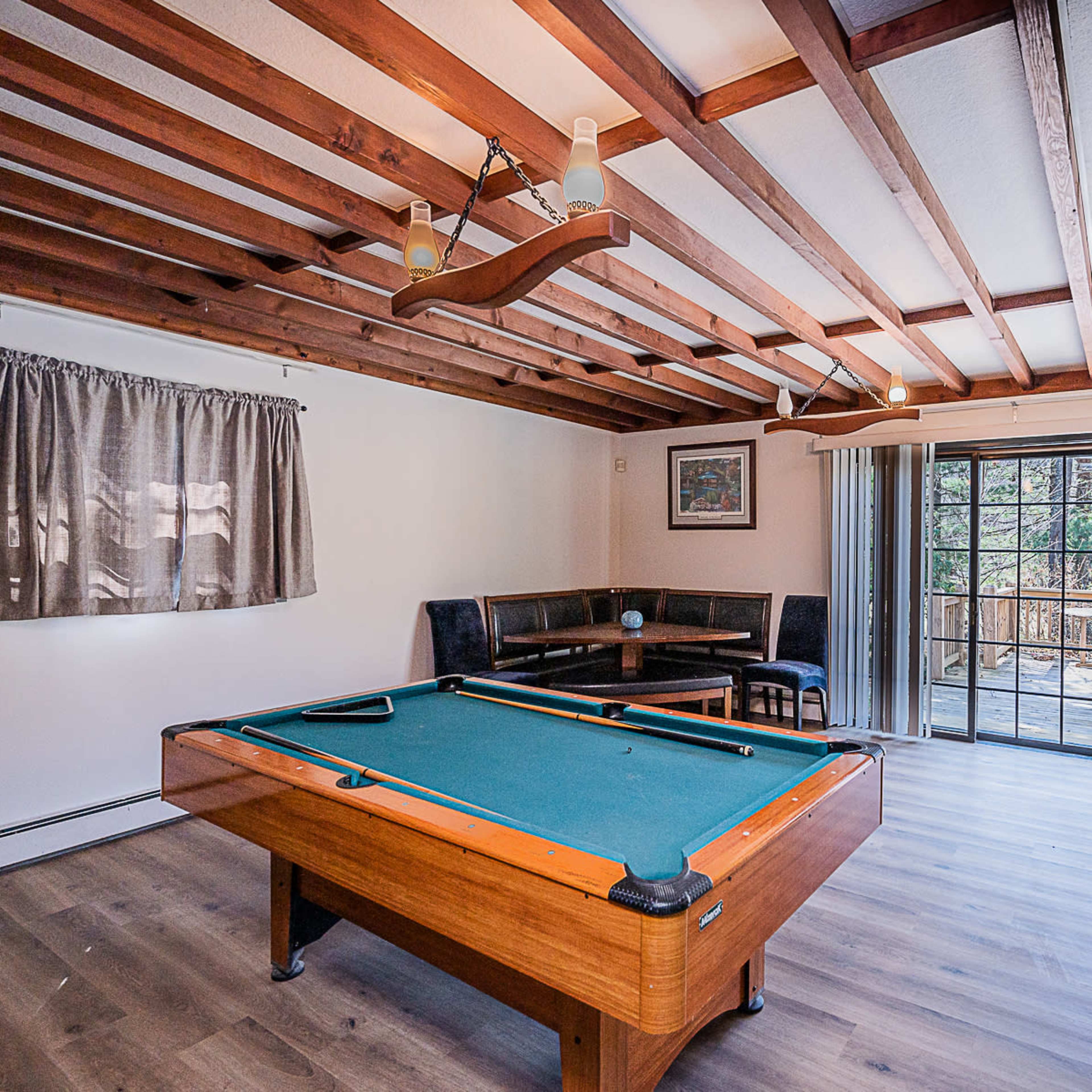 A room with a wooden ceiling, a pool table in the center, a seating area along one wall, and large sliding glass doors leading to an outdoor deck.