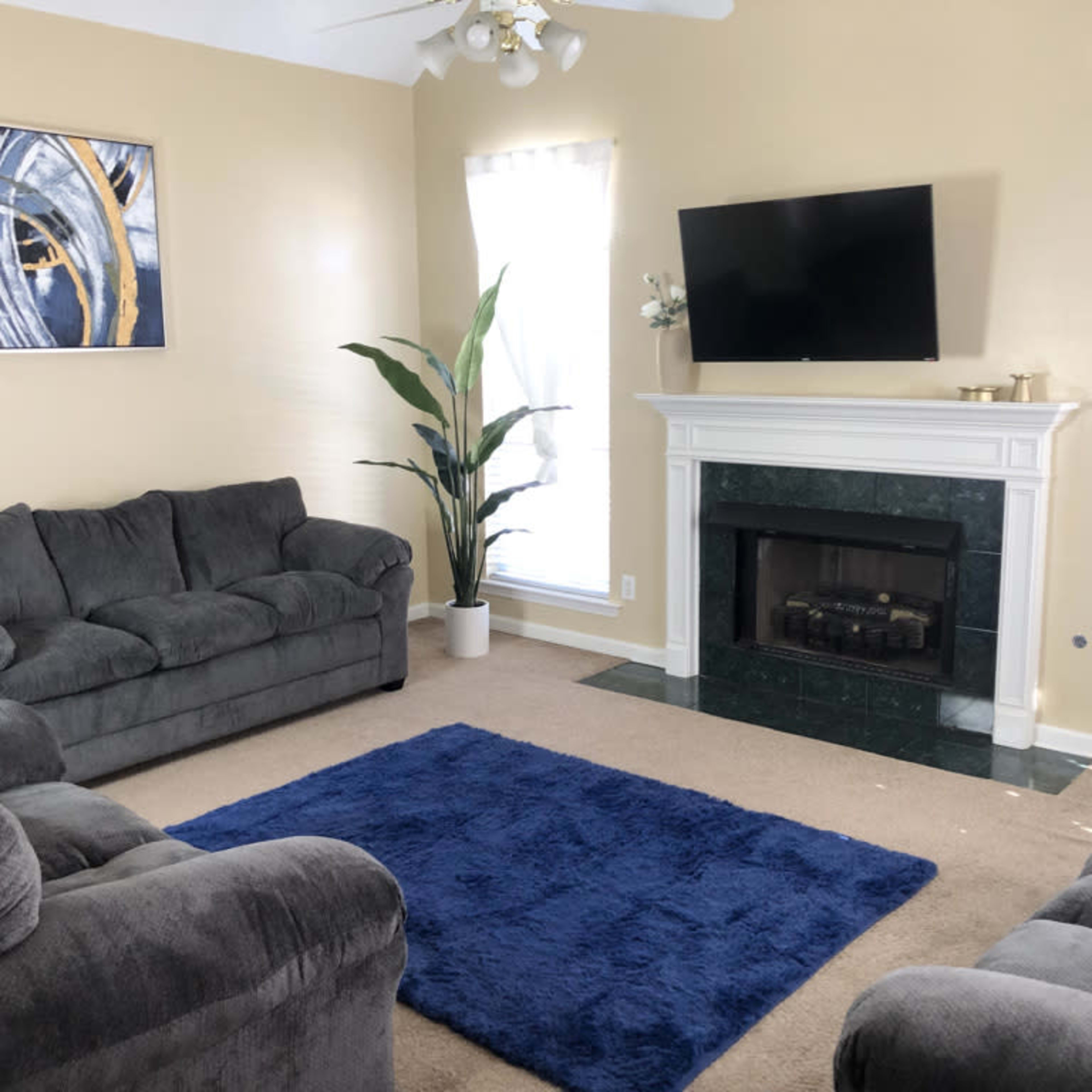 A living room with two gray sofas, a blue area rug, a marble fireplace, and a mounted television on a light yellow wall.