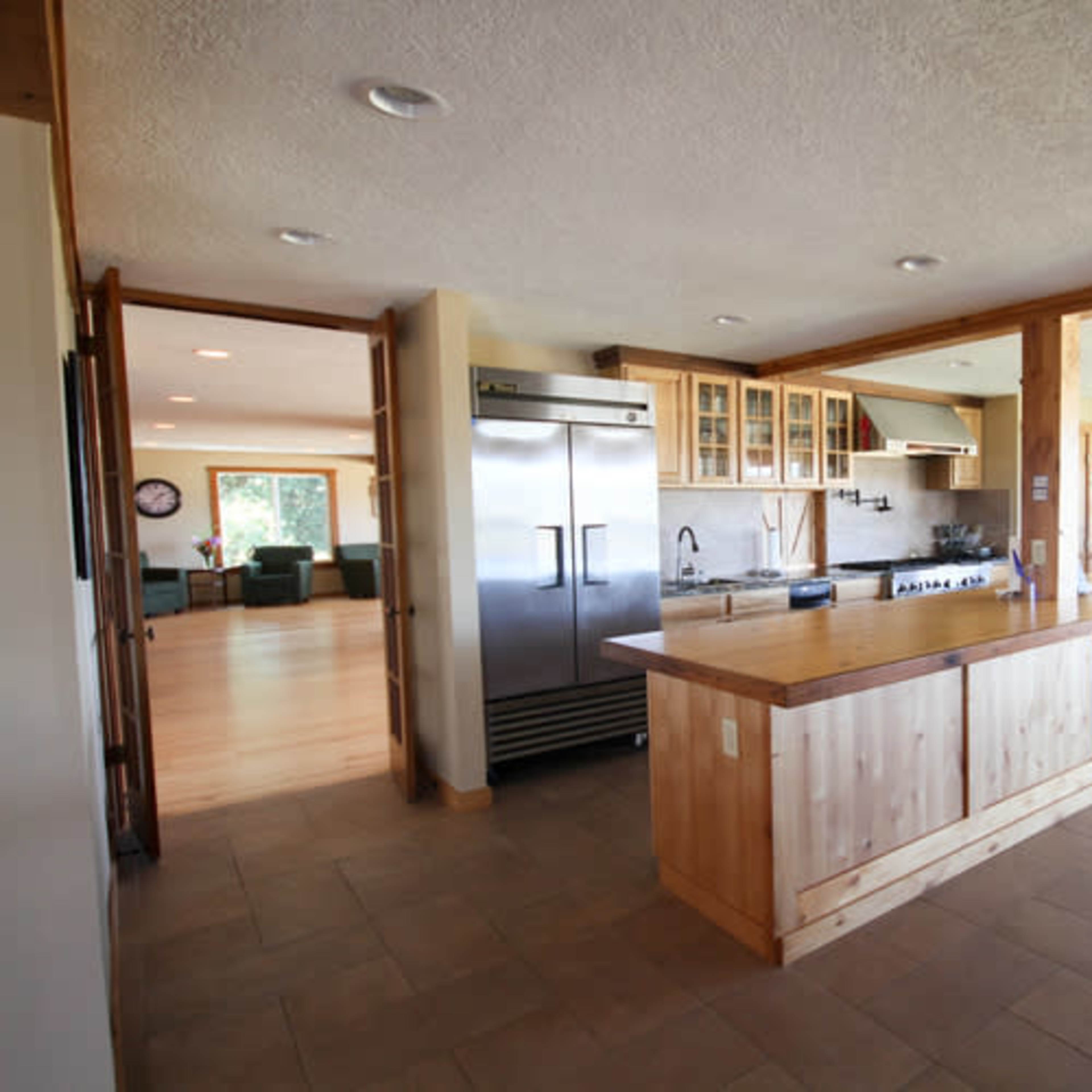 A modern kitchen with a large island, stainless steel appliances, and wood cabinetry, connected to an open living space.