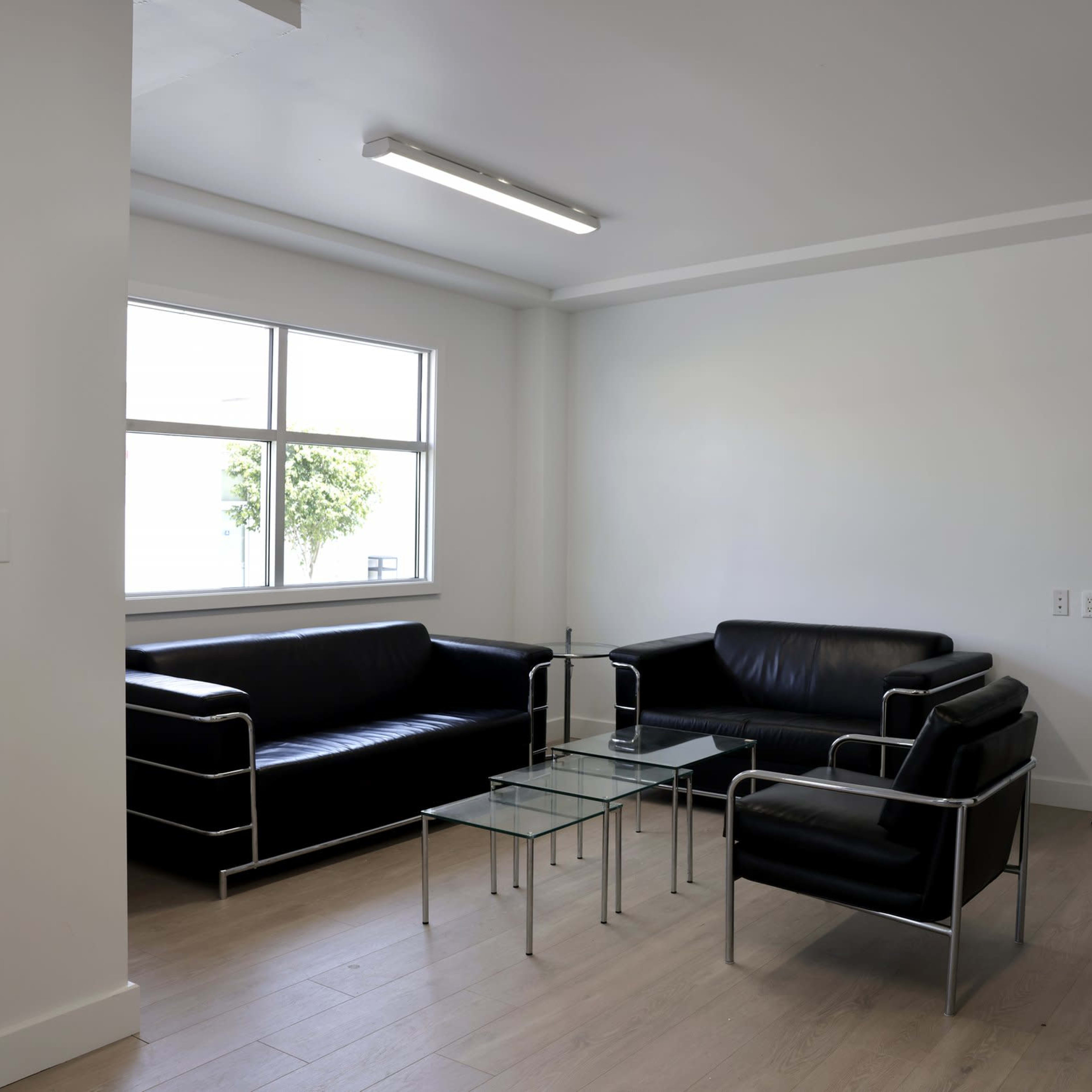 A modern living space features two black sofas, a glass coffee table, and a large floor lamp near a window.