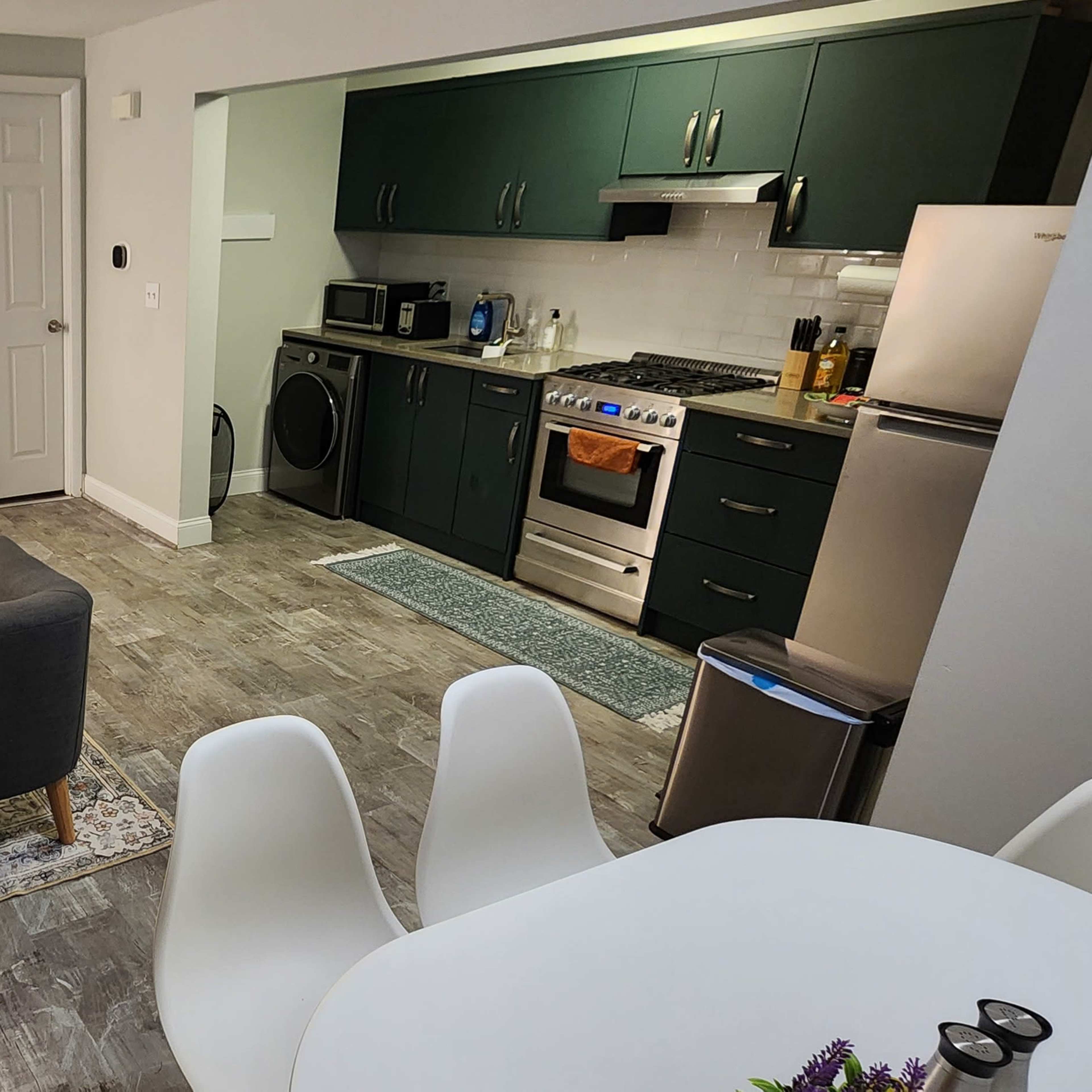 A modern interior of a living space featuring a kitchen with appliances, a dining area, and a cozy seating area with a gray sofa and light-colored furniture.