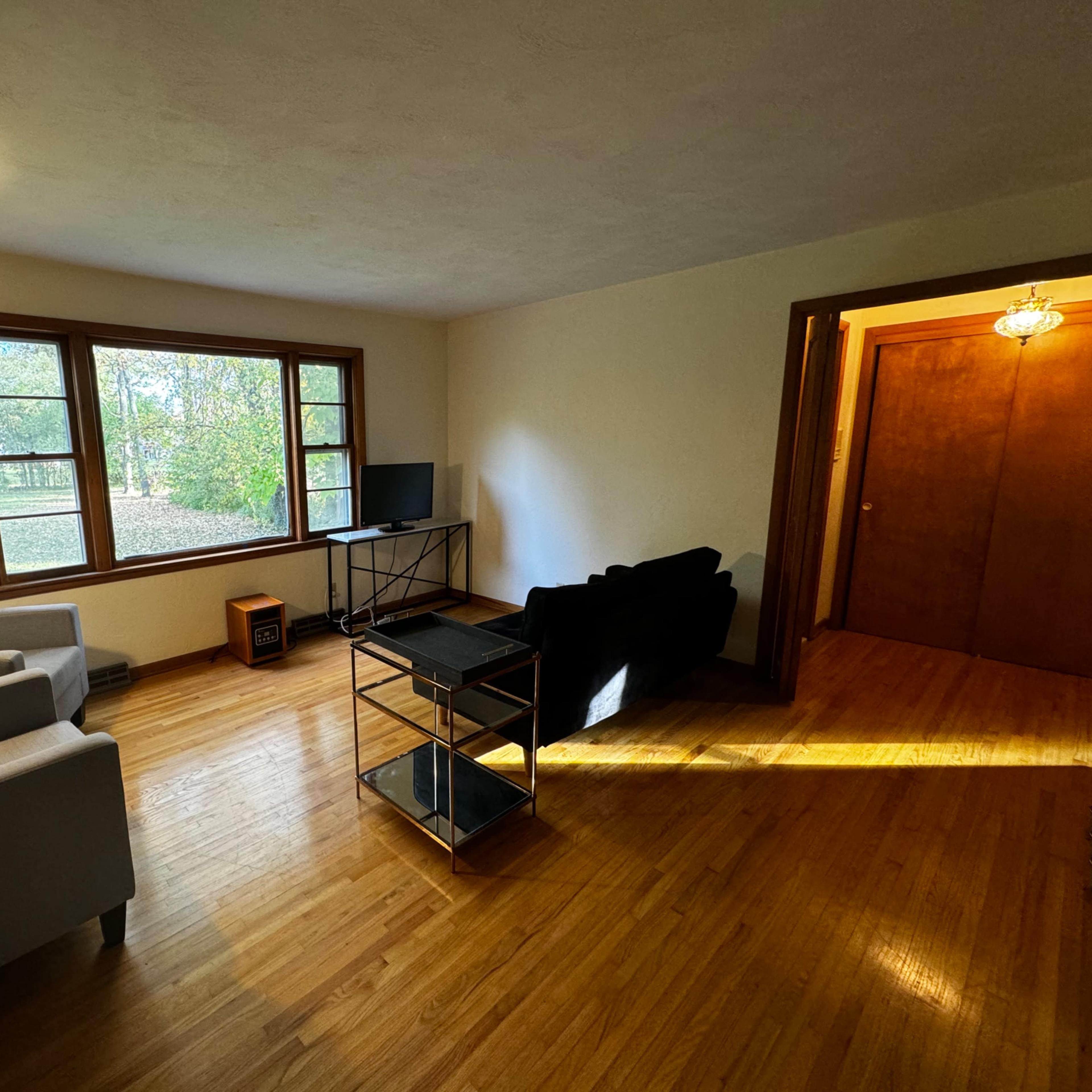 The room features two chairs, a small table, a television on a stand, and a large window with a view of the outdoors.