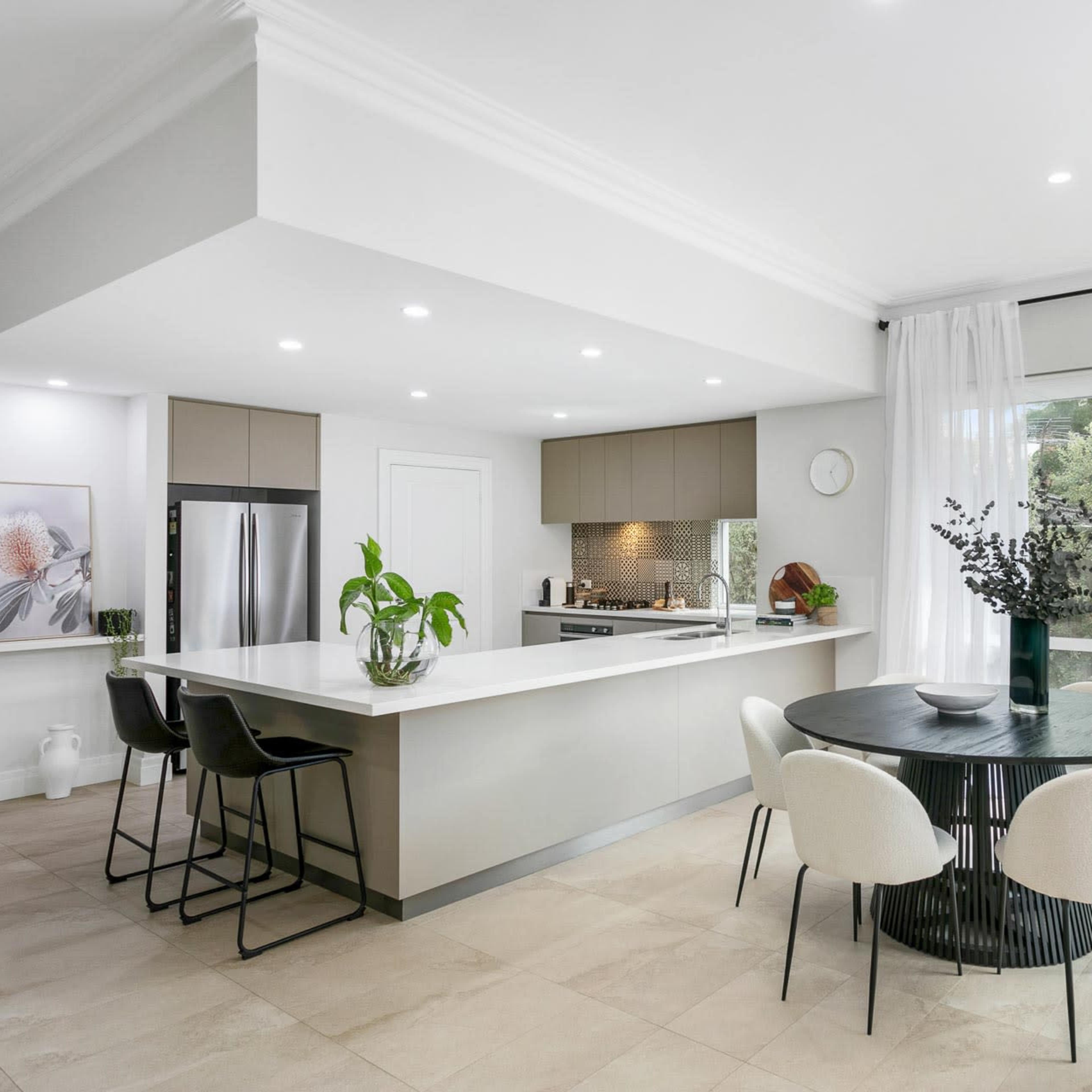 A modern kitchen and dining area with a circular table, four chairs, and large windows allowing natural light to enter.