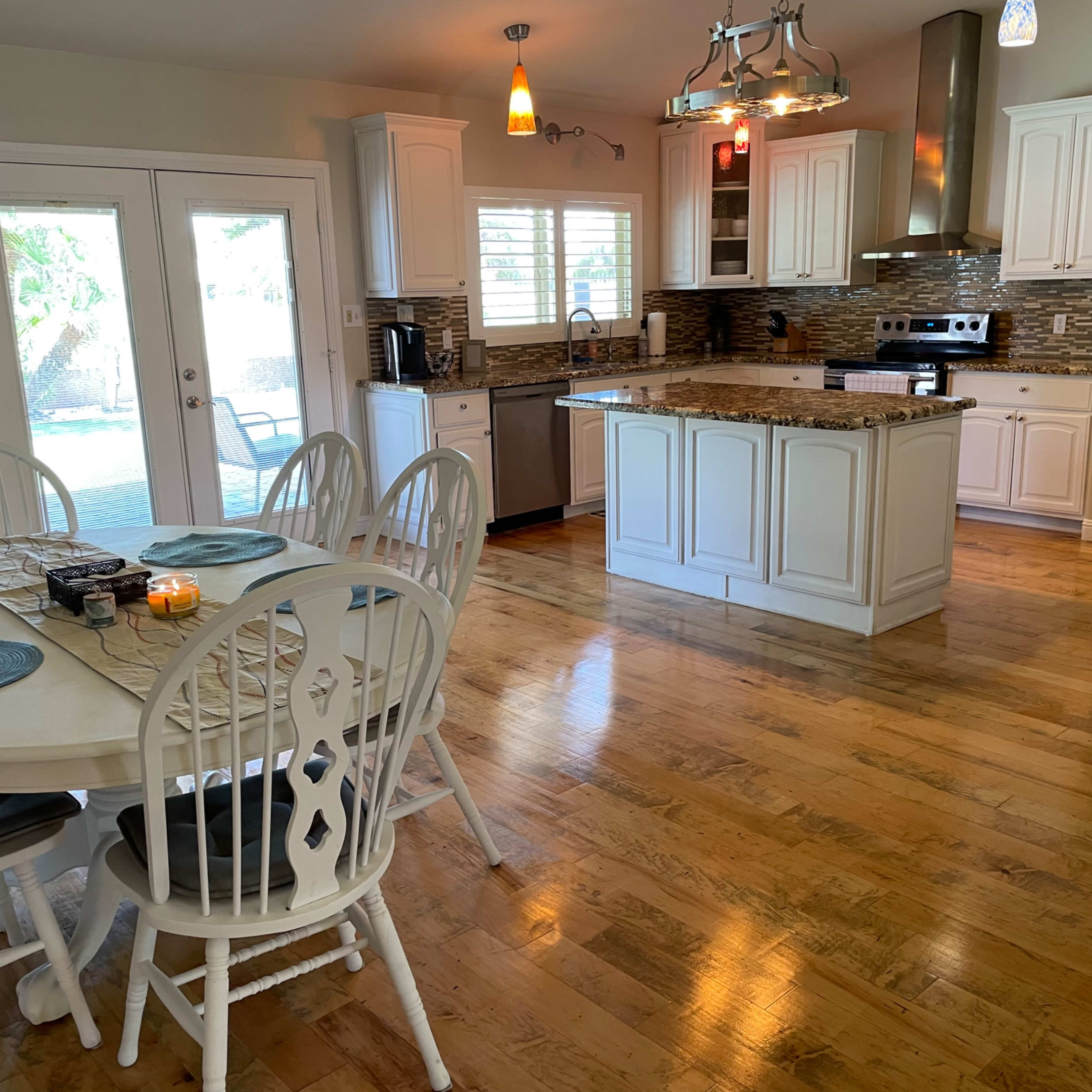 A bright kitchen and dining area with a round table set for six, featuring white cabinetry and granite countertops.