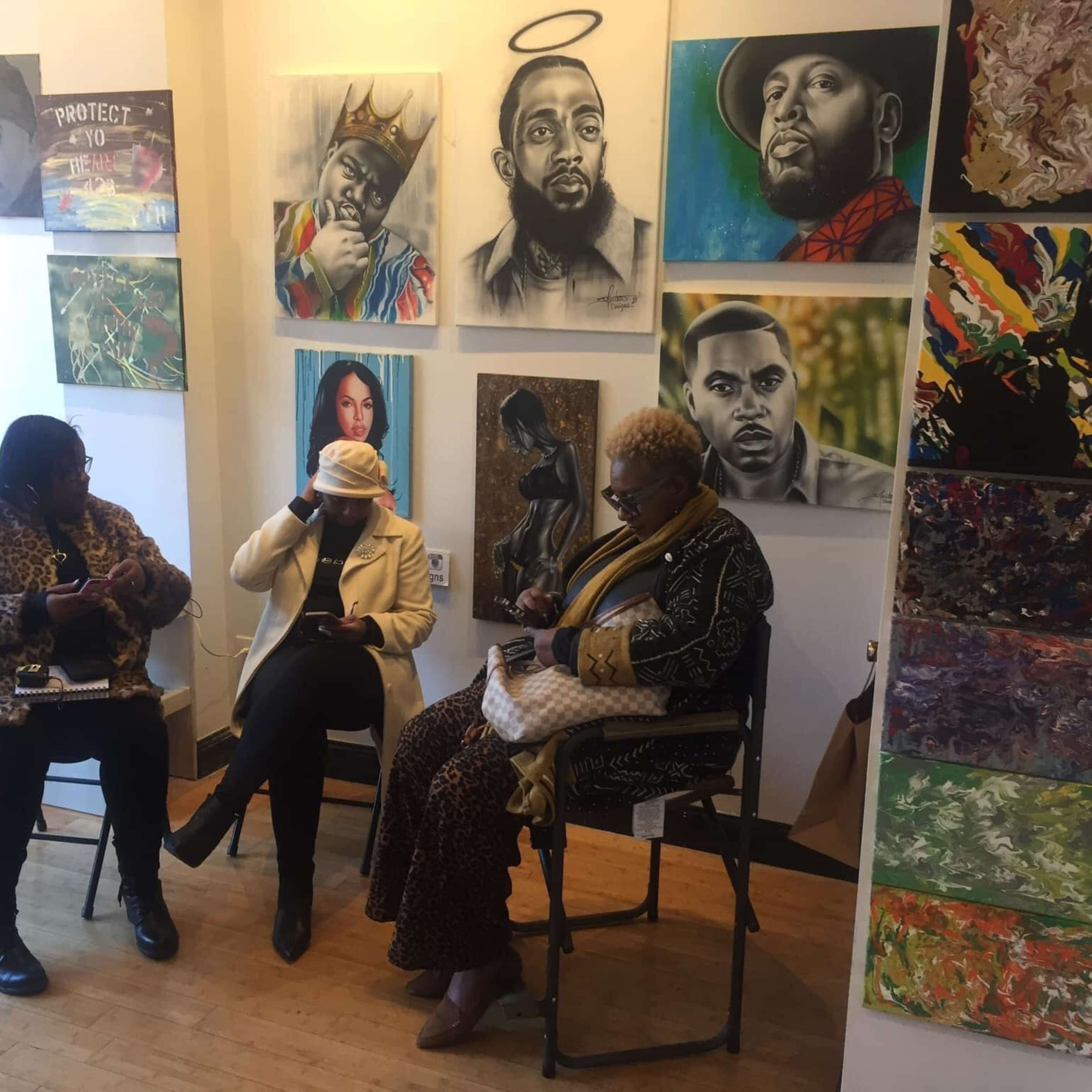 Three women sit in a gallery adorned with various paintings and portraits, focused on their phones.
