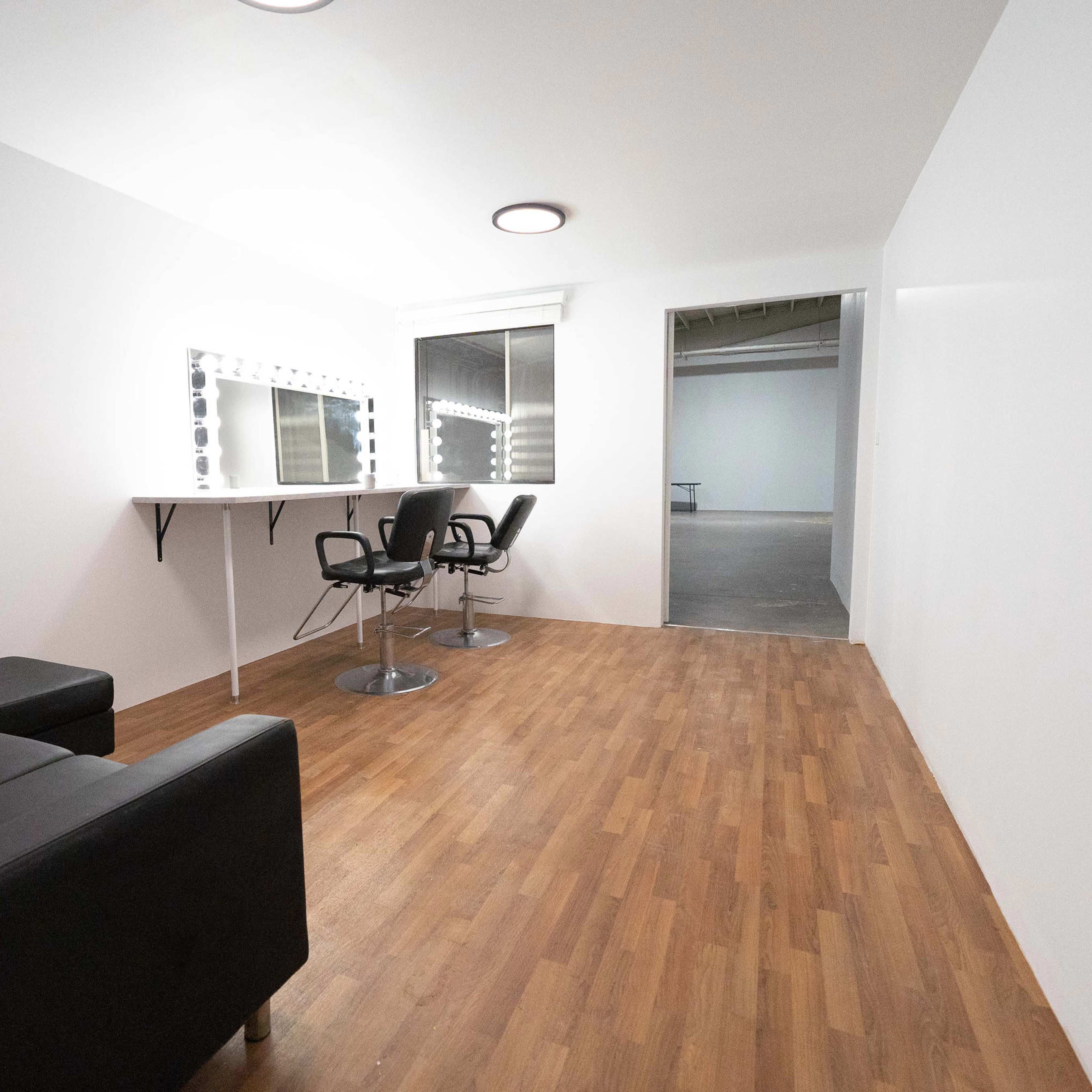 A minimalist room with a mirrored vanity and two black chairs, a black sofa, and a doorway leading to another space.