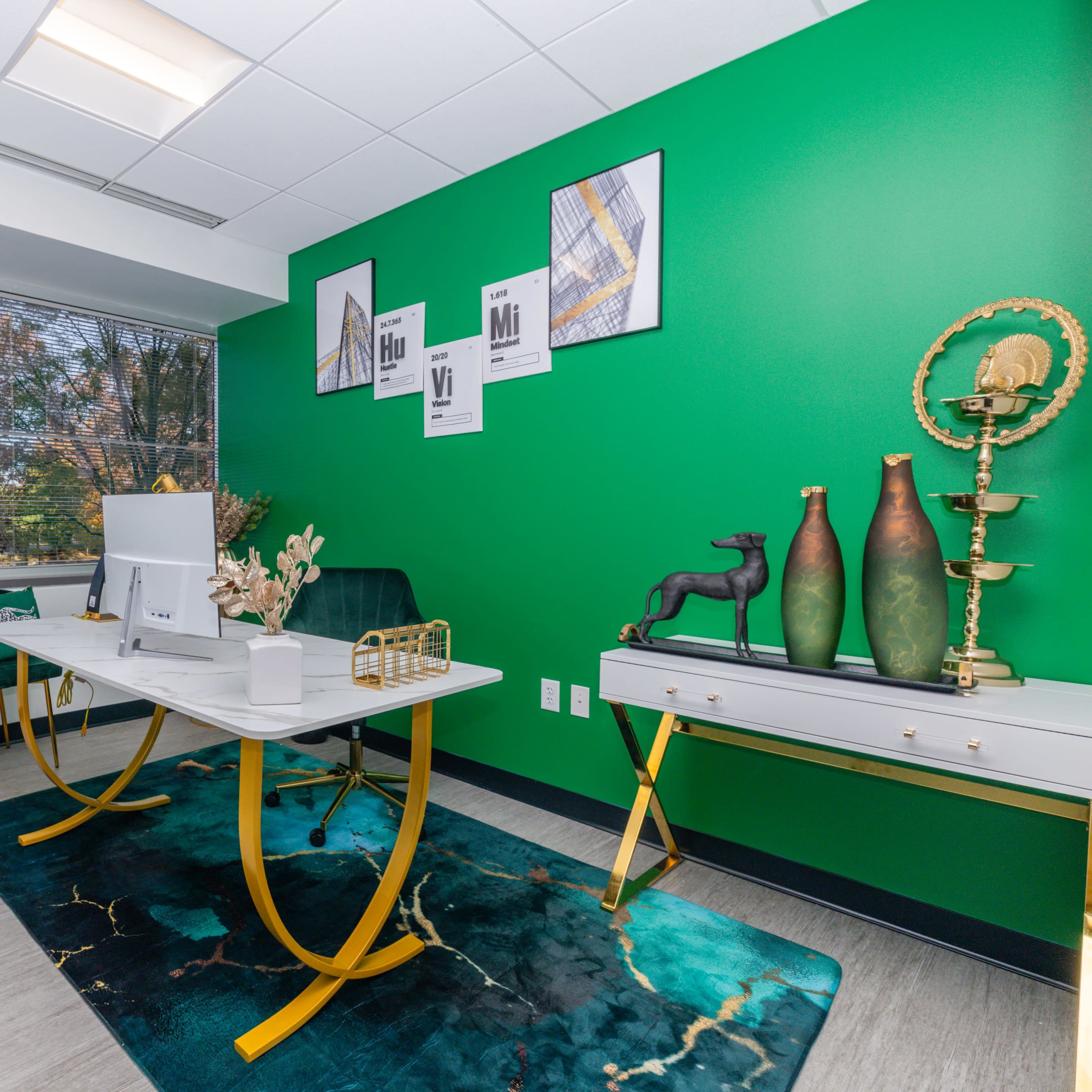 A modern office with a green accent wall, a white desk, and stylish decor including a rug, vases, and artwork on the walls.