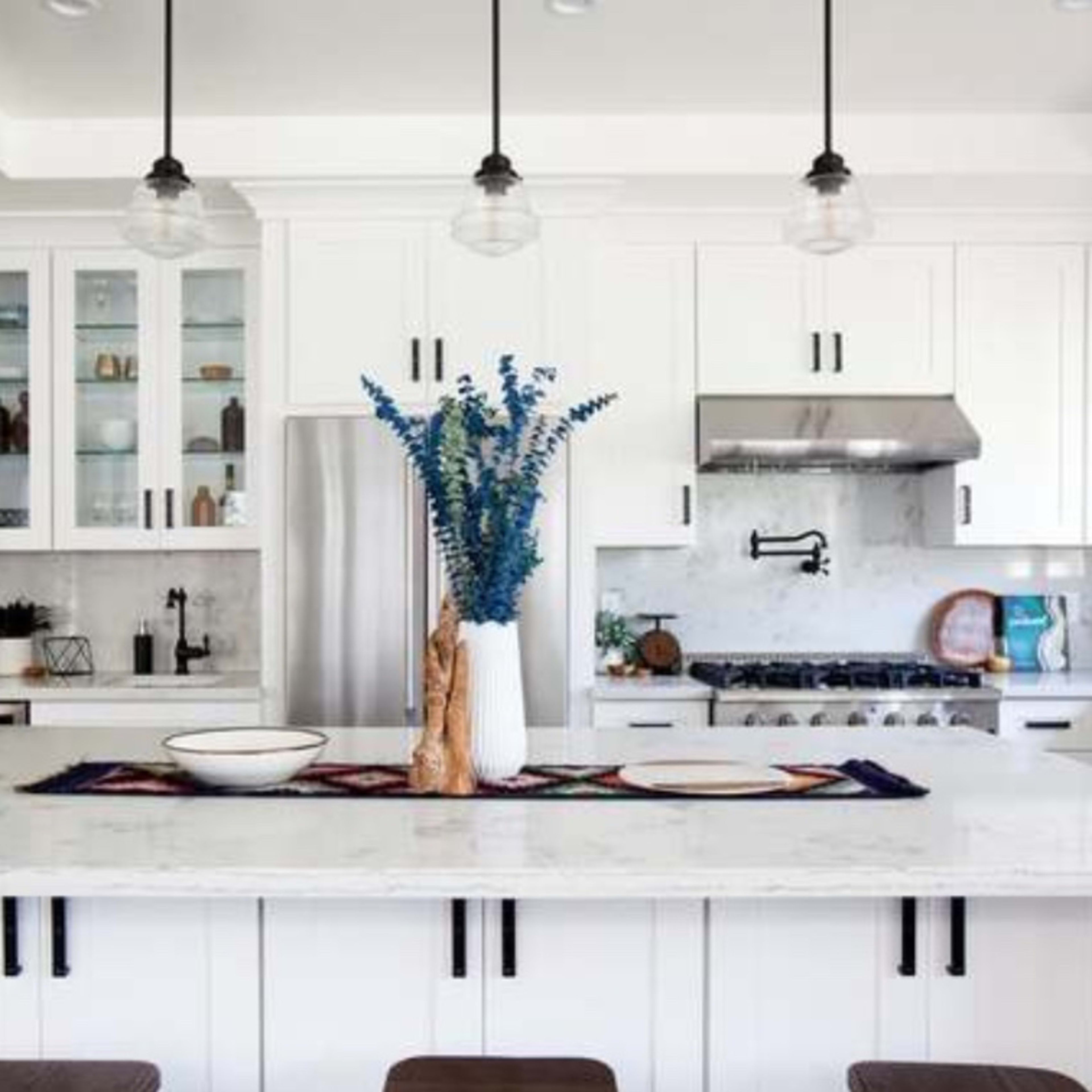 The kitchen features white cabinets, a large marble island with seating, and pendant lighting above.