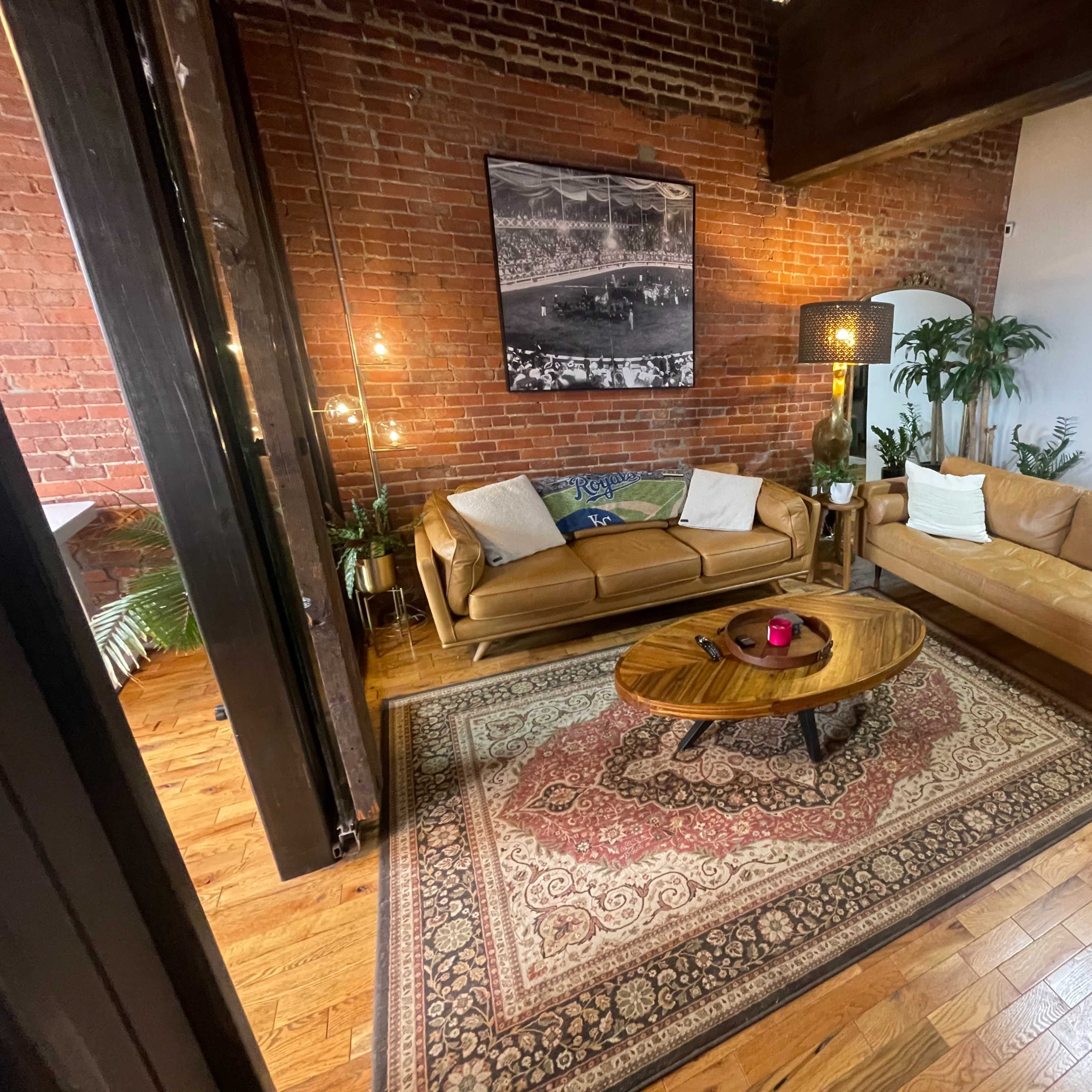 A cozy living room with exposed brick walls, two leather sofas, a circular wooden coffee table, and a patterned rug.