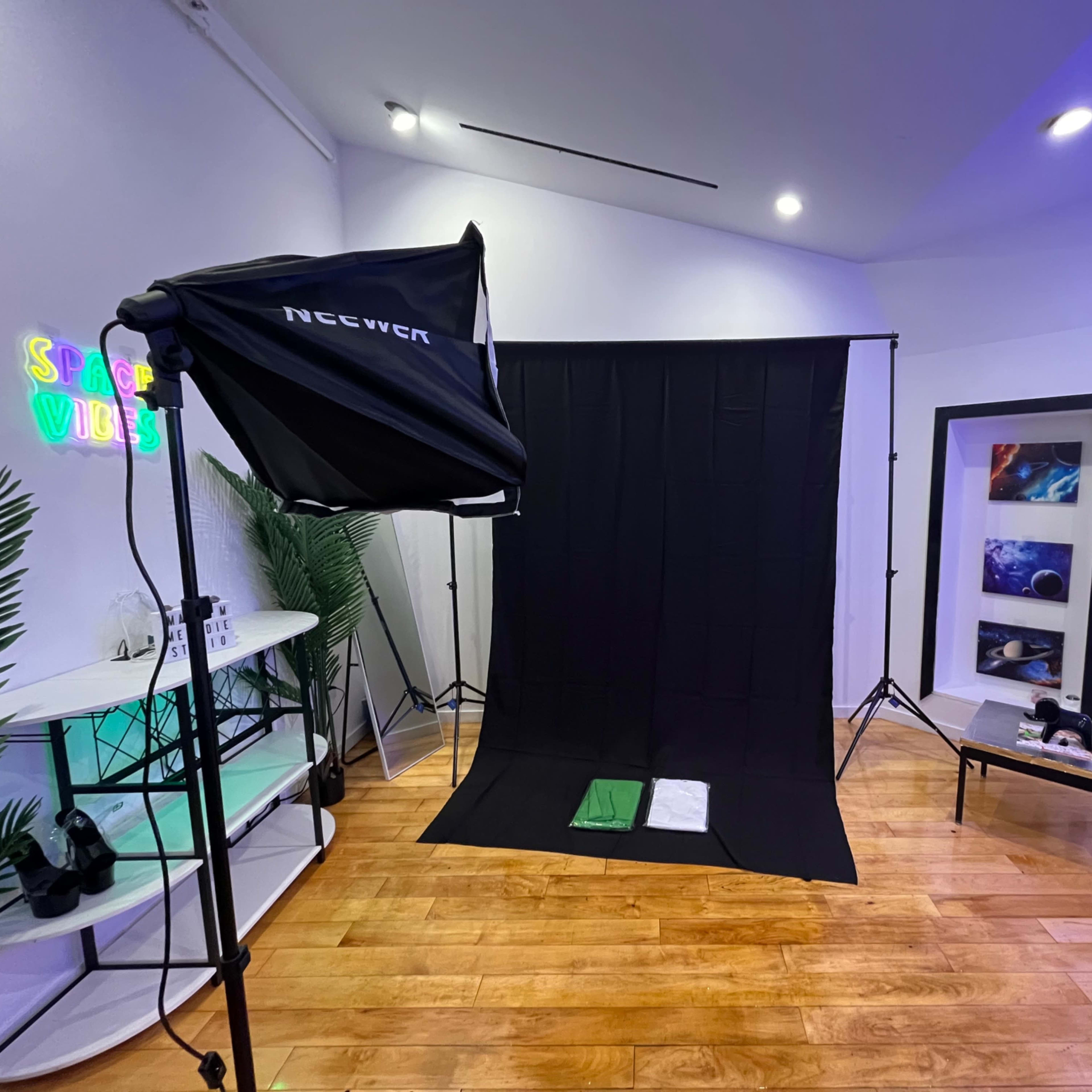 A photography studio setup with a black backdrop, a lighting softbox, and various props arranged on a nearby table.