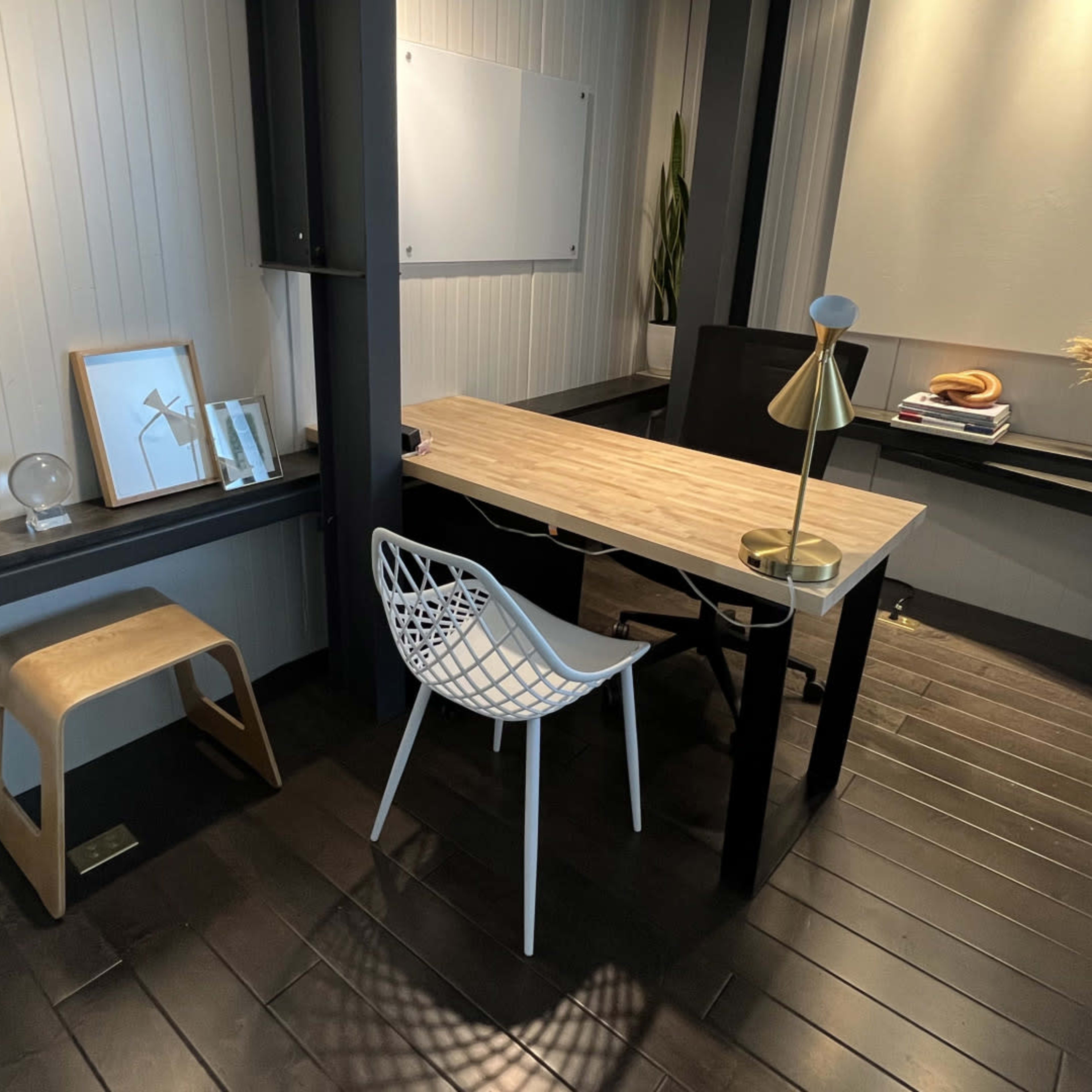 A modern, minimalist office space with a wooden table, a white chair, and decorative elements on the walls and surfaces.