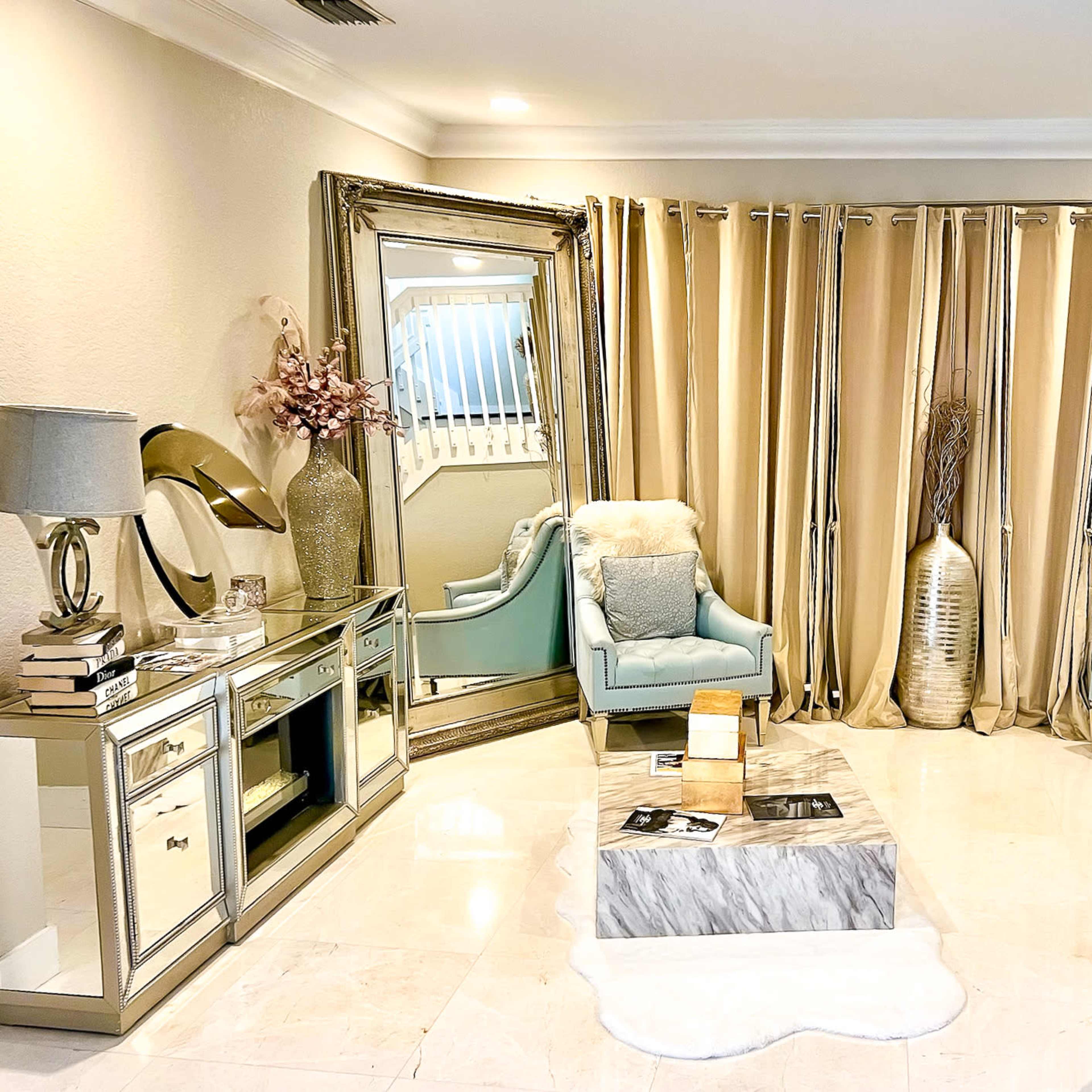 The living room features two light blue chairs, a gray sofa, a decorative mirror, and a marble coffee table, all arranged around a plush white area rug.