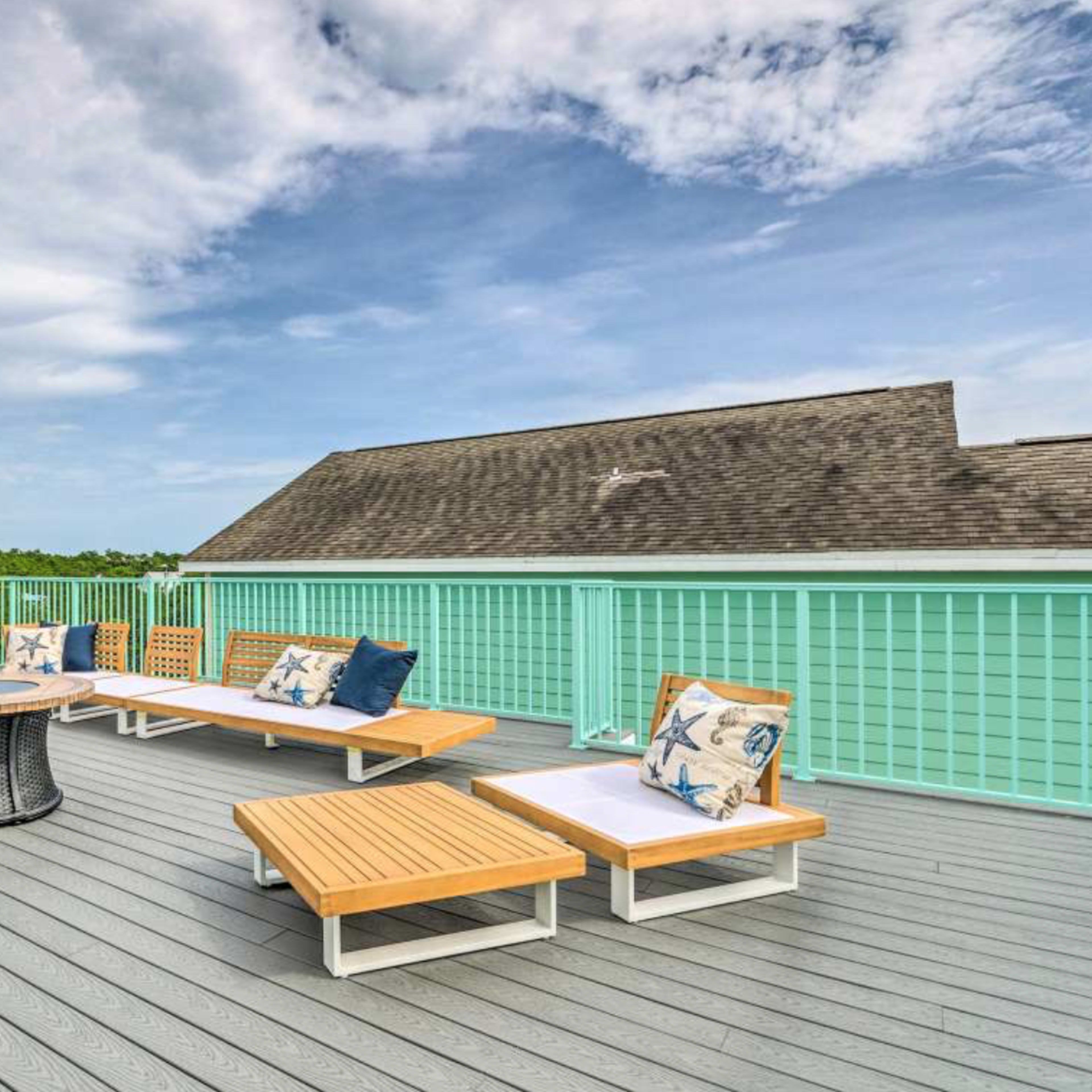 A deck features wooden lounge furniture and a circular table, overlooking a green landscape under a partly cloudy sky.