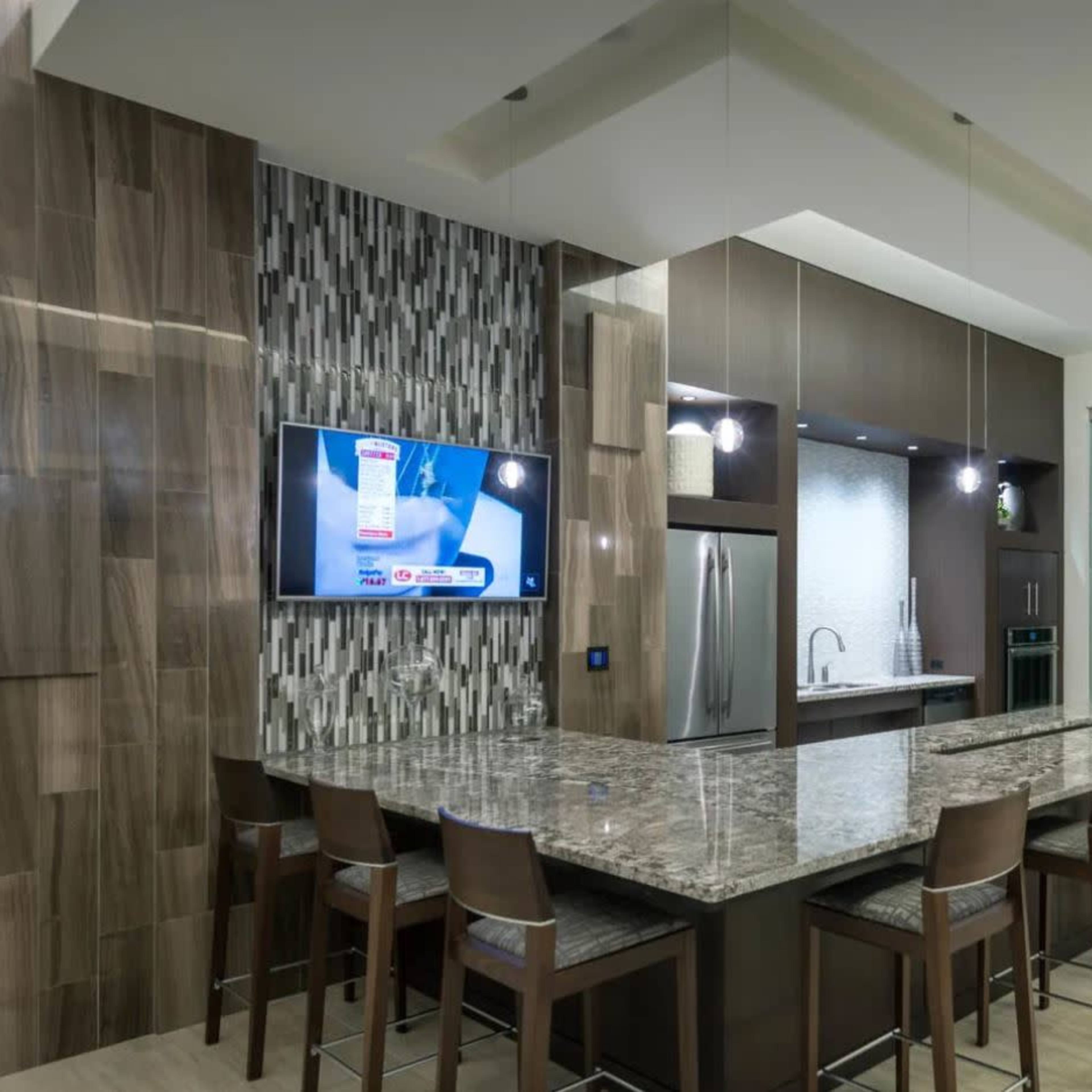 A modern kitchen with a large granite island, a wall-mounted television, and sleek cabinetry.