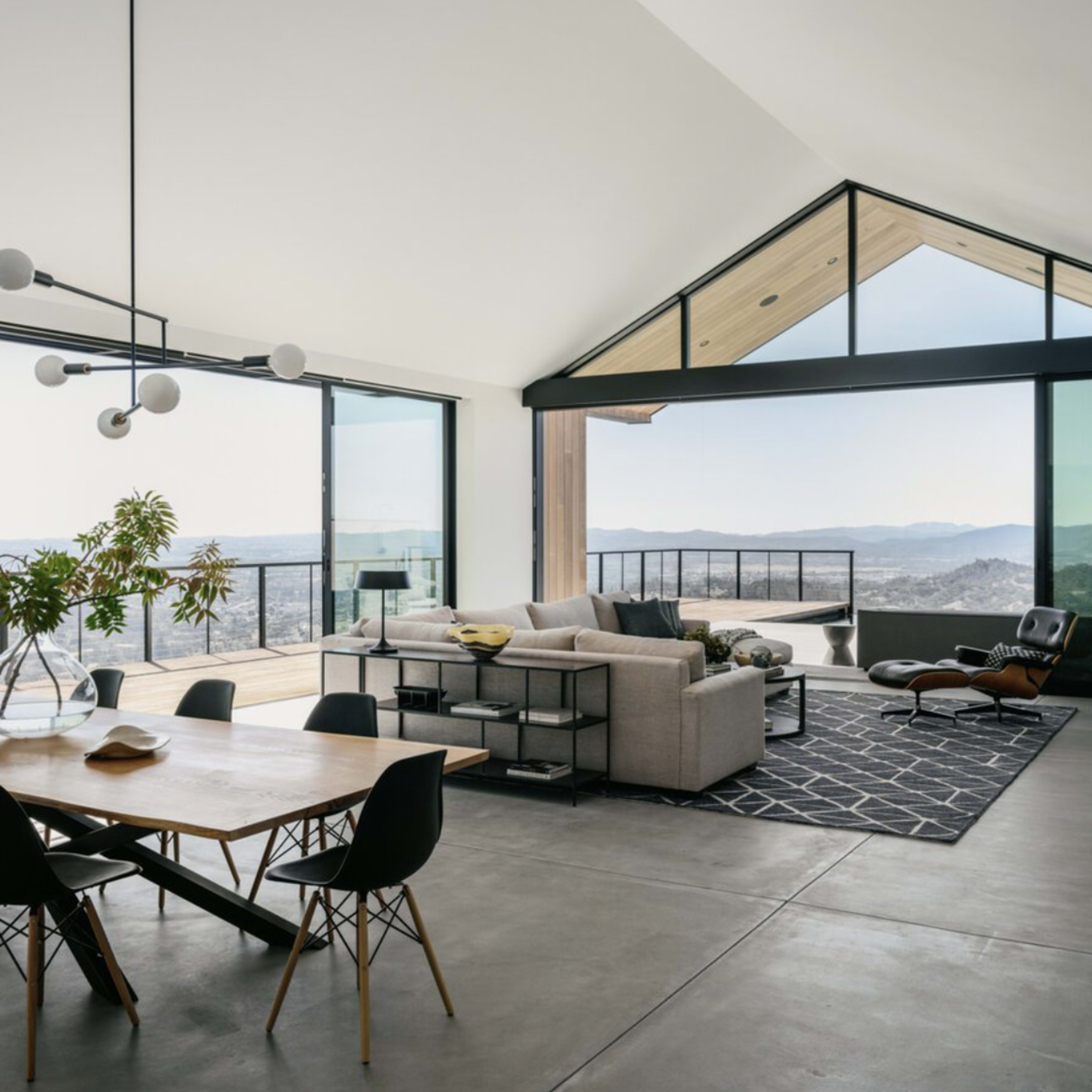 A modern living space with a dining area, a sofa, and large windows offering a view of a distant landscape.