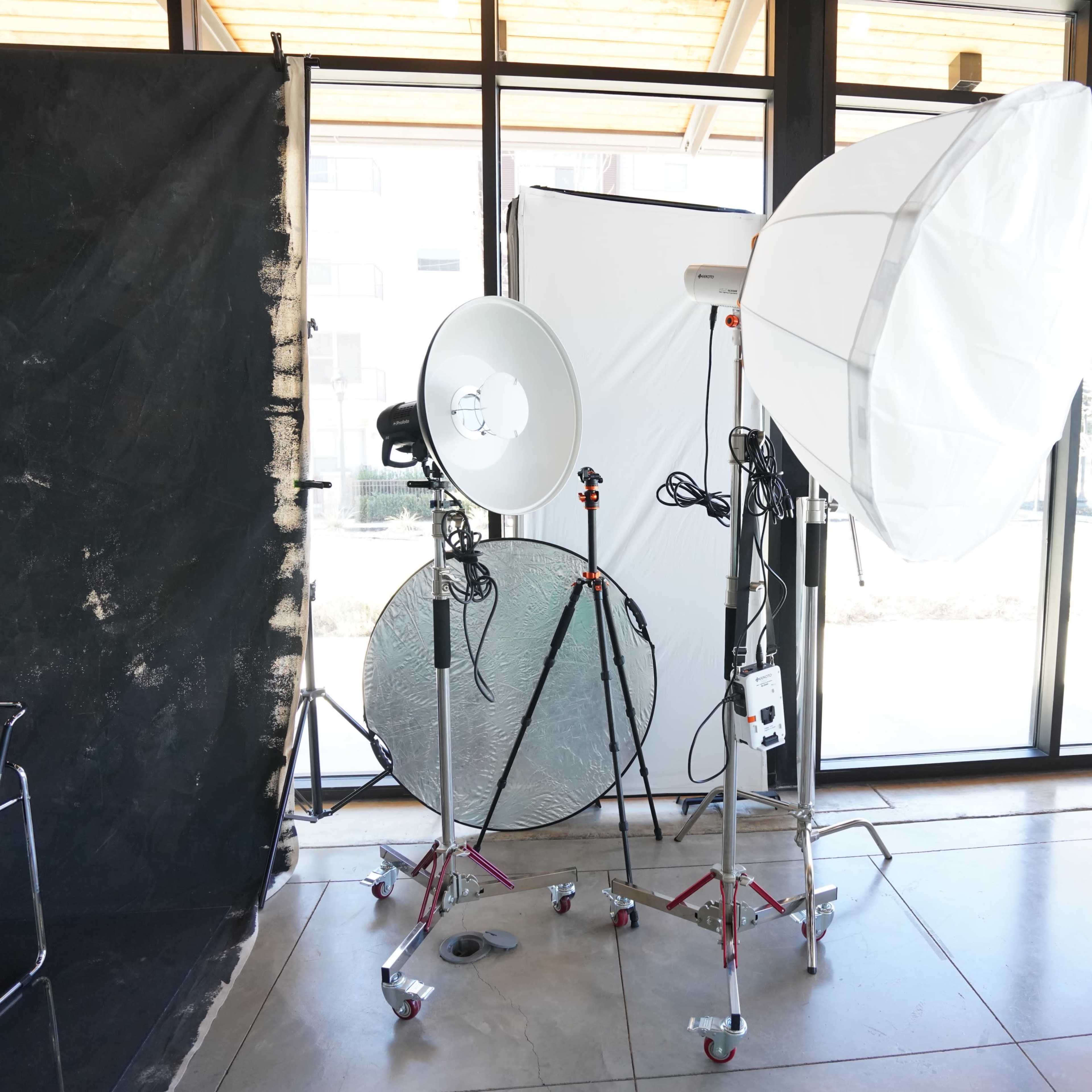 A photography setup with two lighting equipment setups, a reflector, and a backdrop in a well-lit interior space.