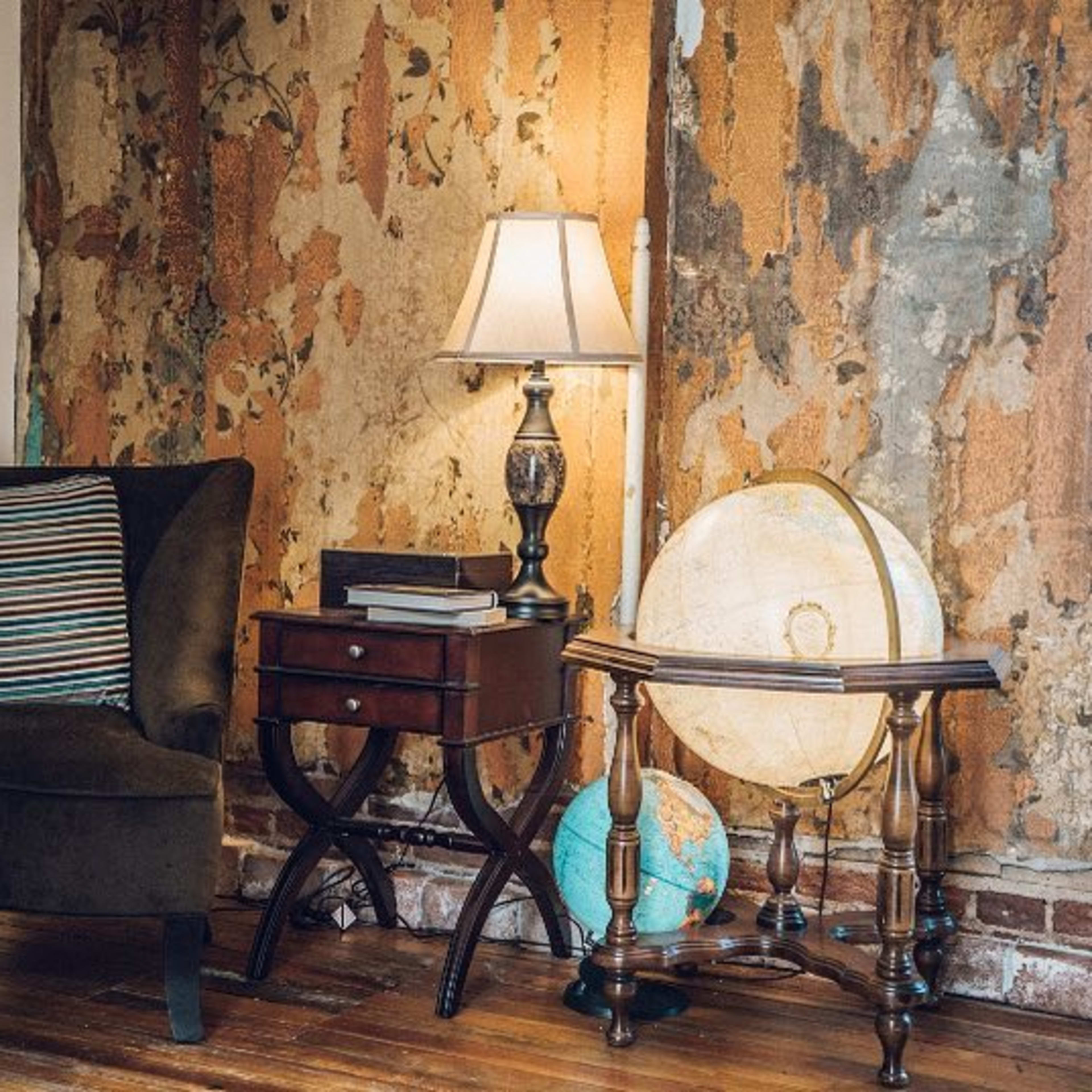 A cozy corner featuring a brown armchair, a lamp on a side table, and a globe beside an exposed, textured wall.