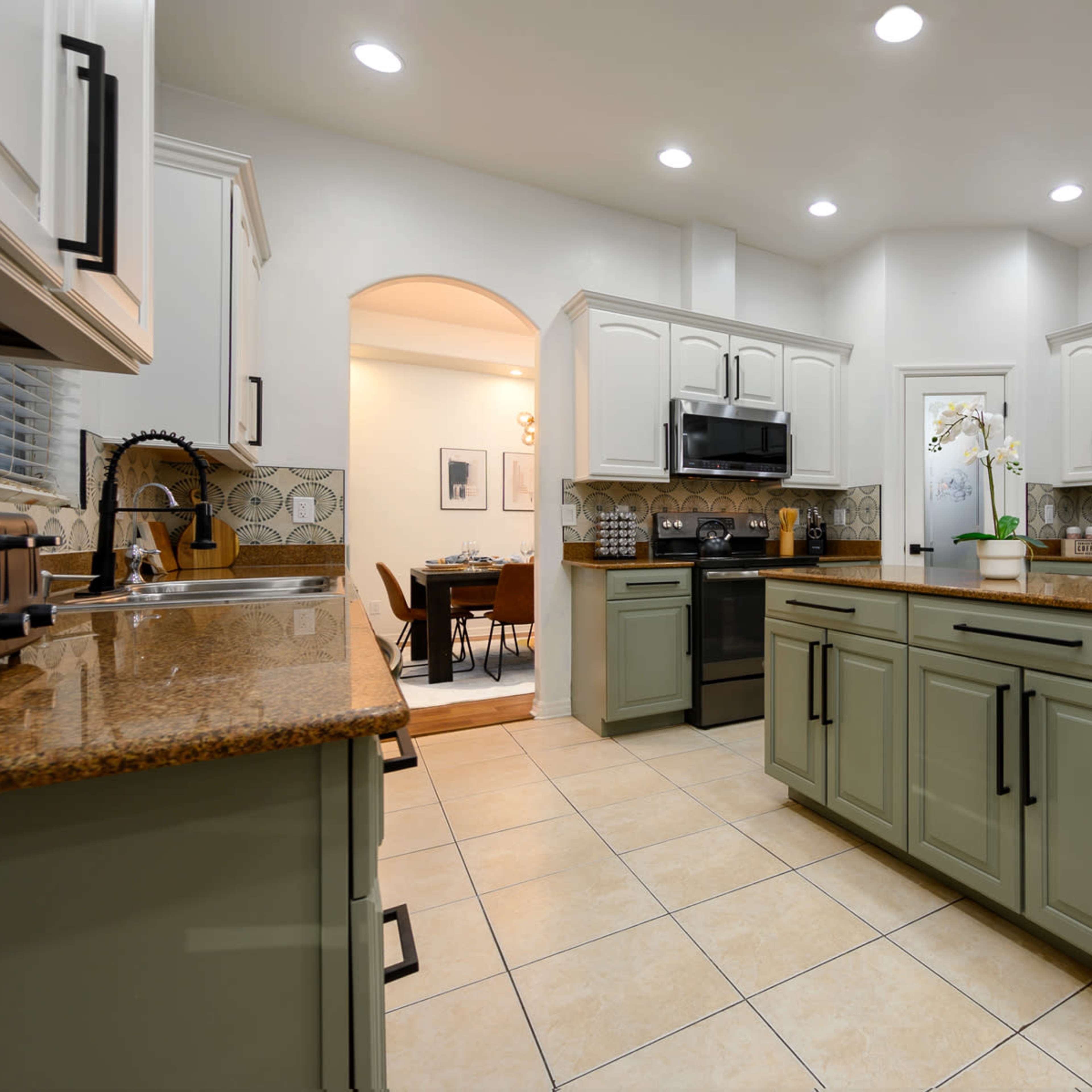 A spacious kitchen features light green cabinetry, a large central island with a granite countertop, and stainless steel appliances.