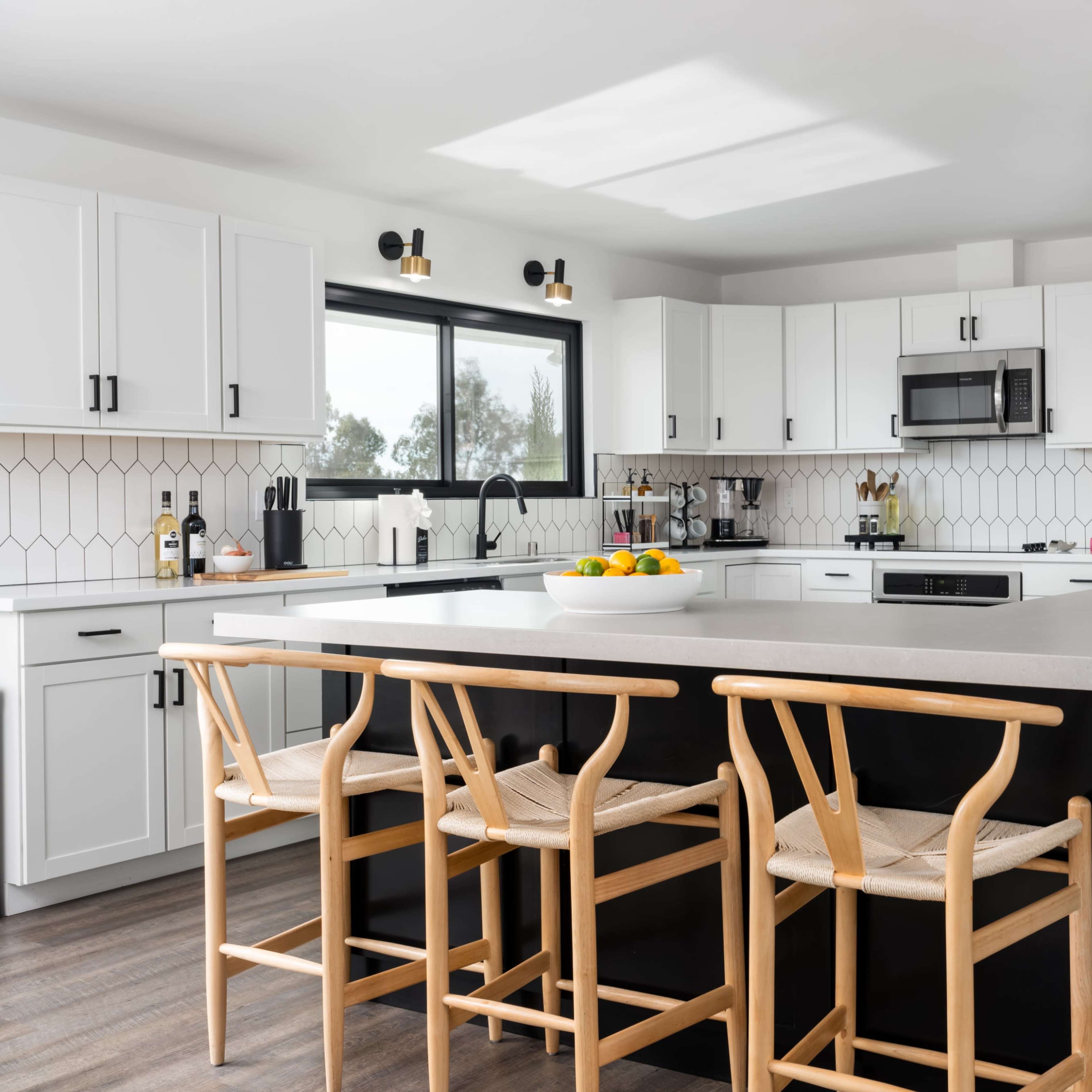 A modern kitchen features white cabinets, a central island with seating, and large windows providing natural light.