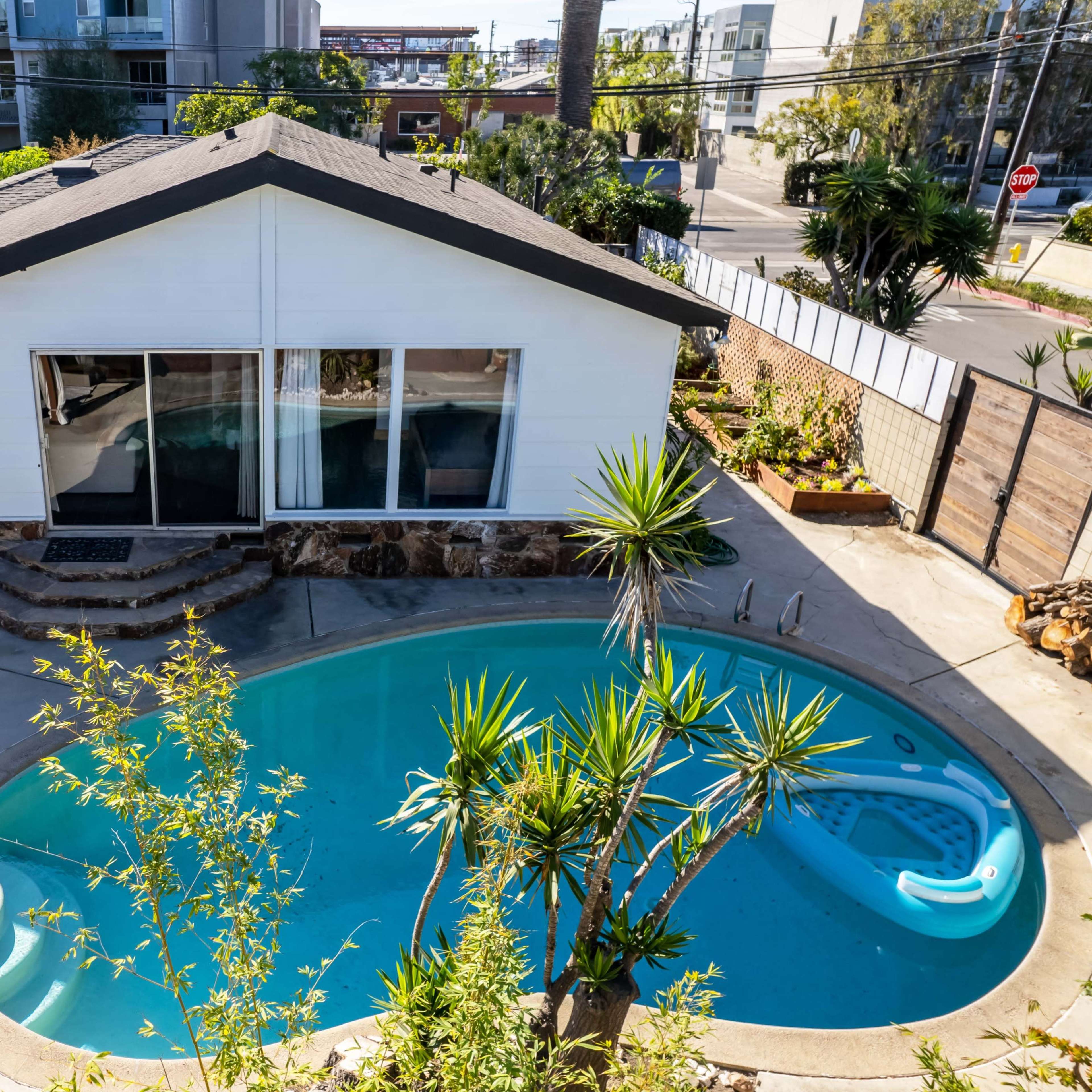 A house with a swimming pool surrounded by plants and a patio area.