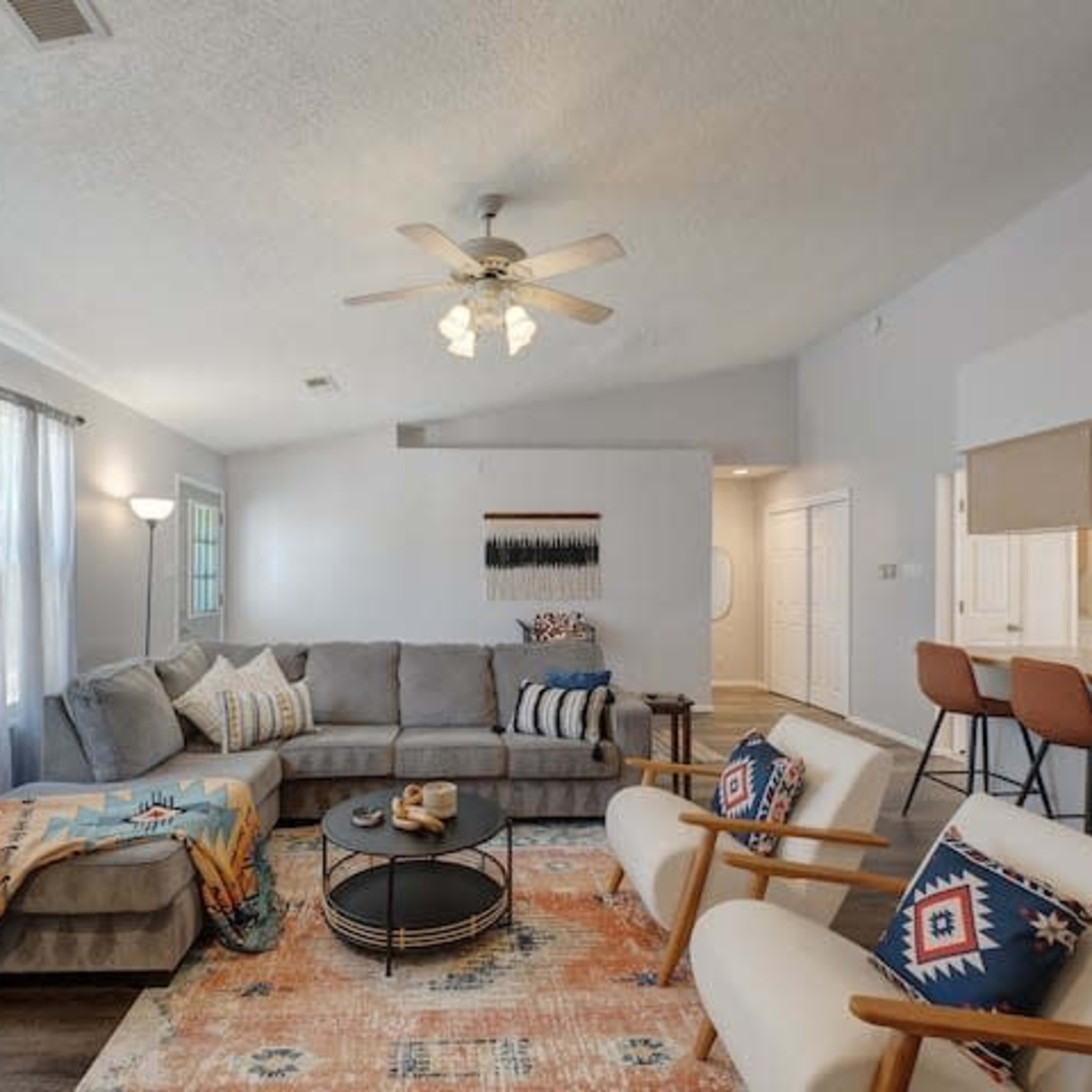A cozy living room featuring a gray sectional sofa, a round coffee table, two armchairs, and a large window with sheer curtains.