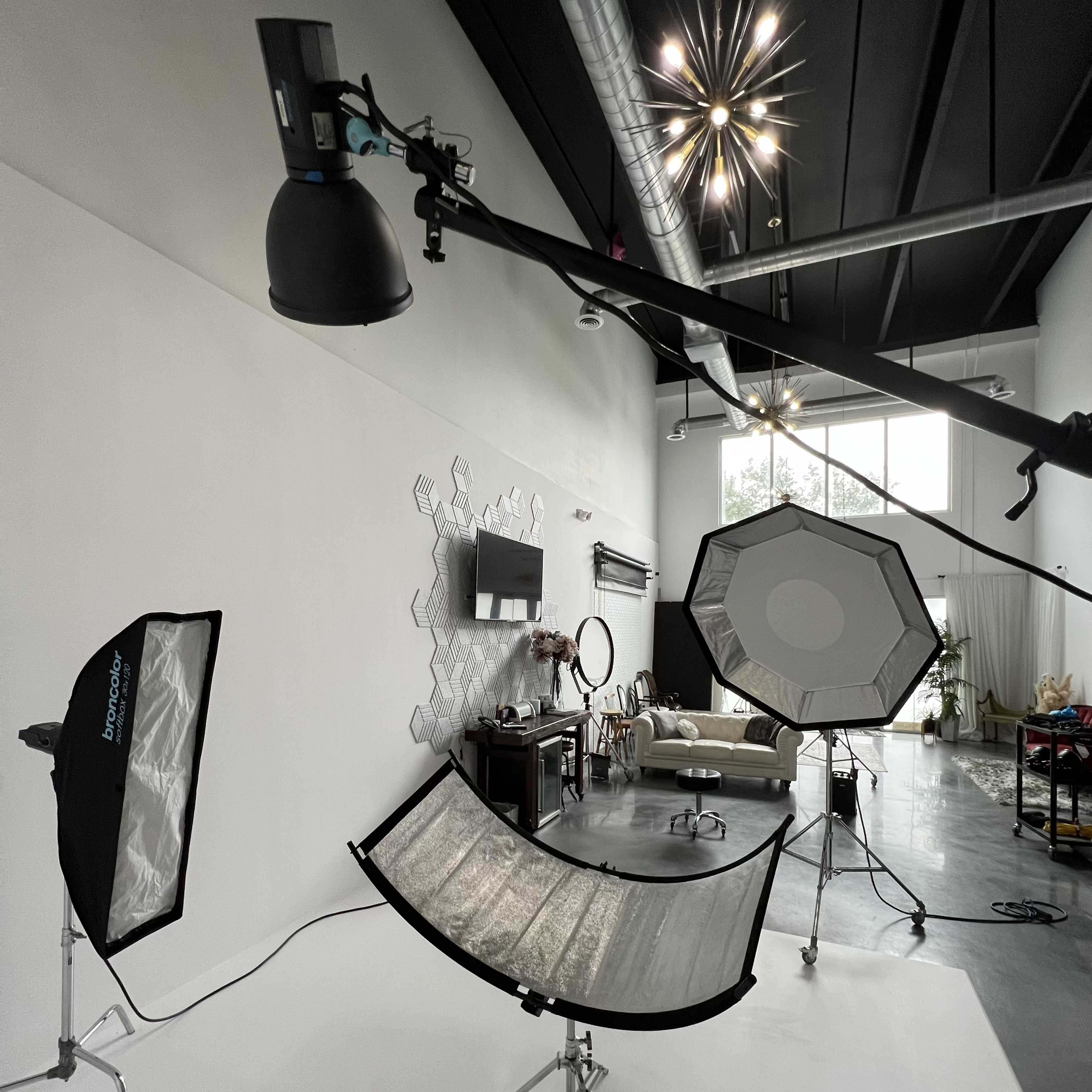 A photography studio is set up with multiple lighting equipment, reflectors, and a backdrop, all ready for a shoot.