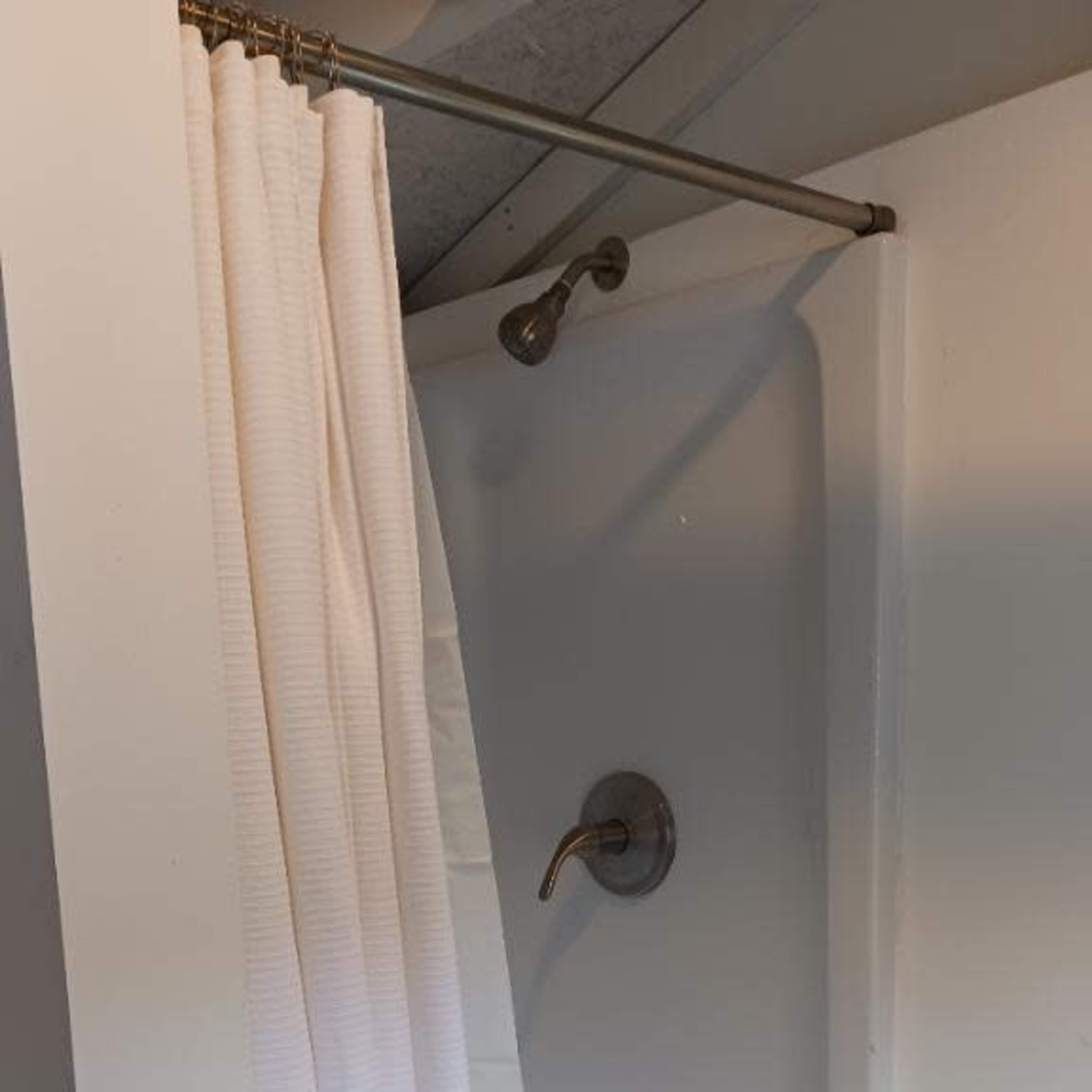 A shower stall with a white curtain partially drawn, revealing a plain showerhead and faucet.