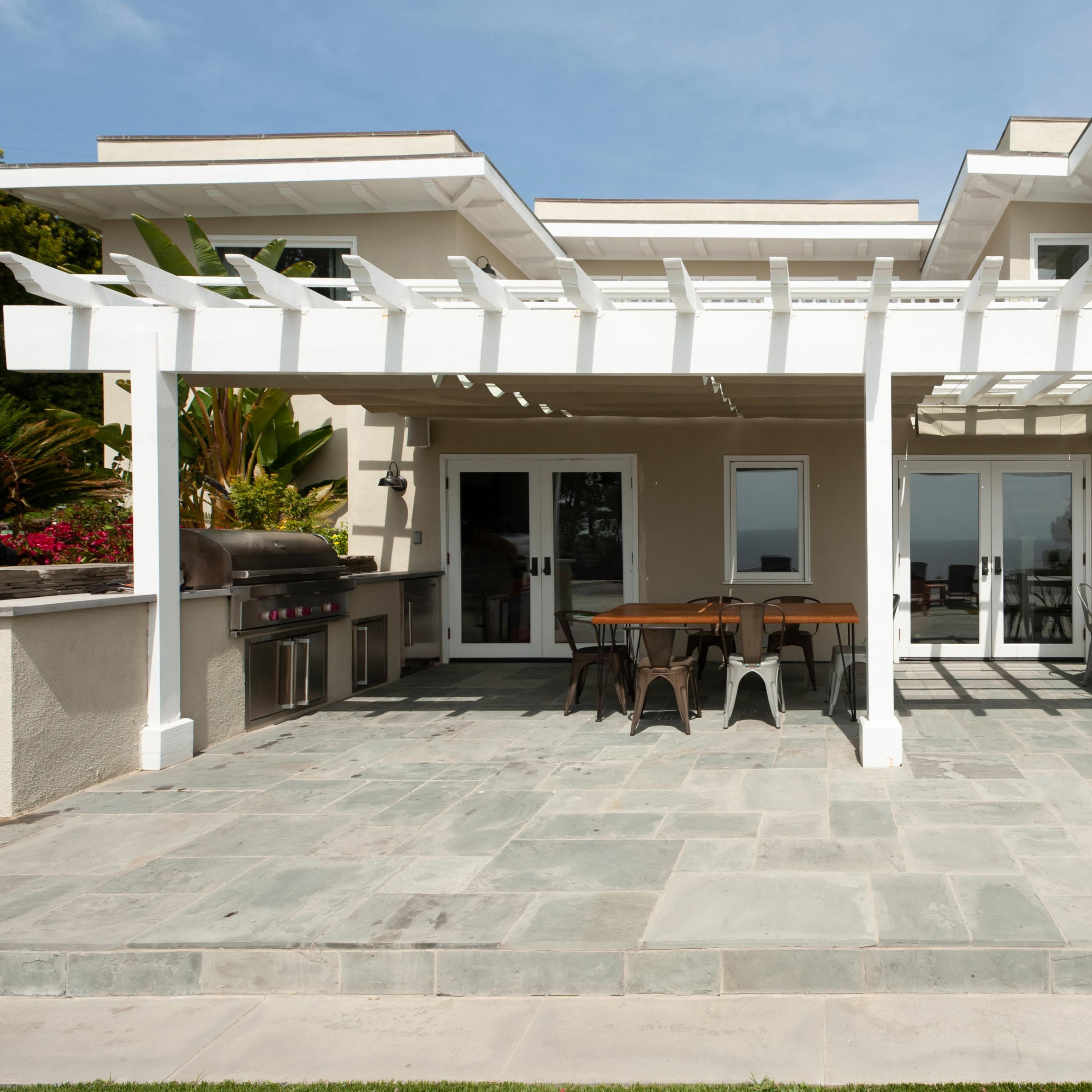 A modern home with a spacious patio featuring a pergola, outdoor furniture, and a barbecue grill.