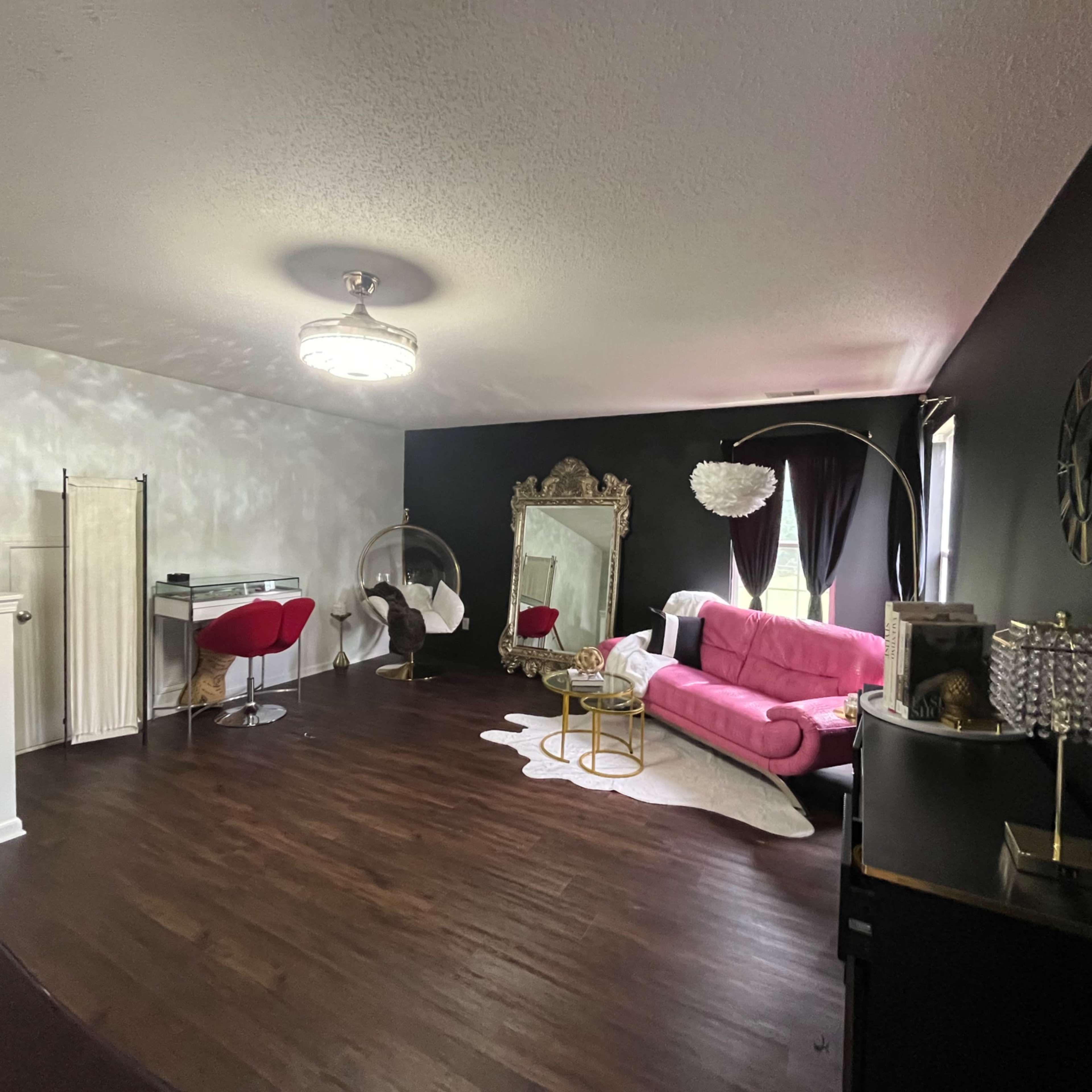 A living room with dark walls, a pink couch, a gold-framed mirror, and various decorative furnishings.