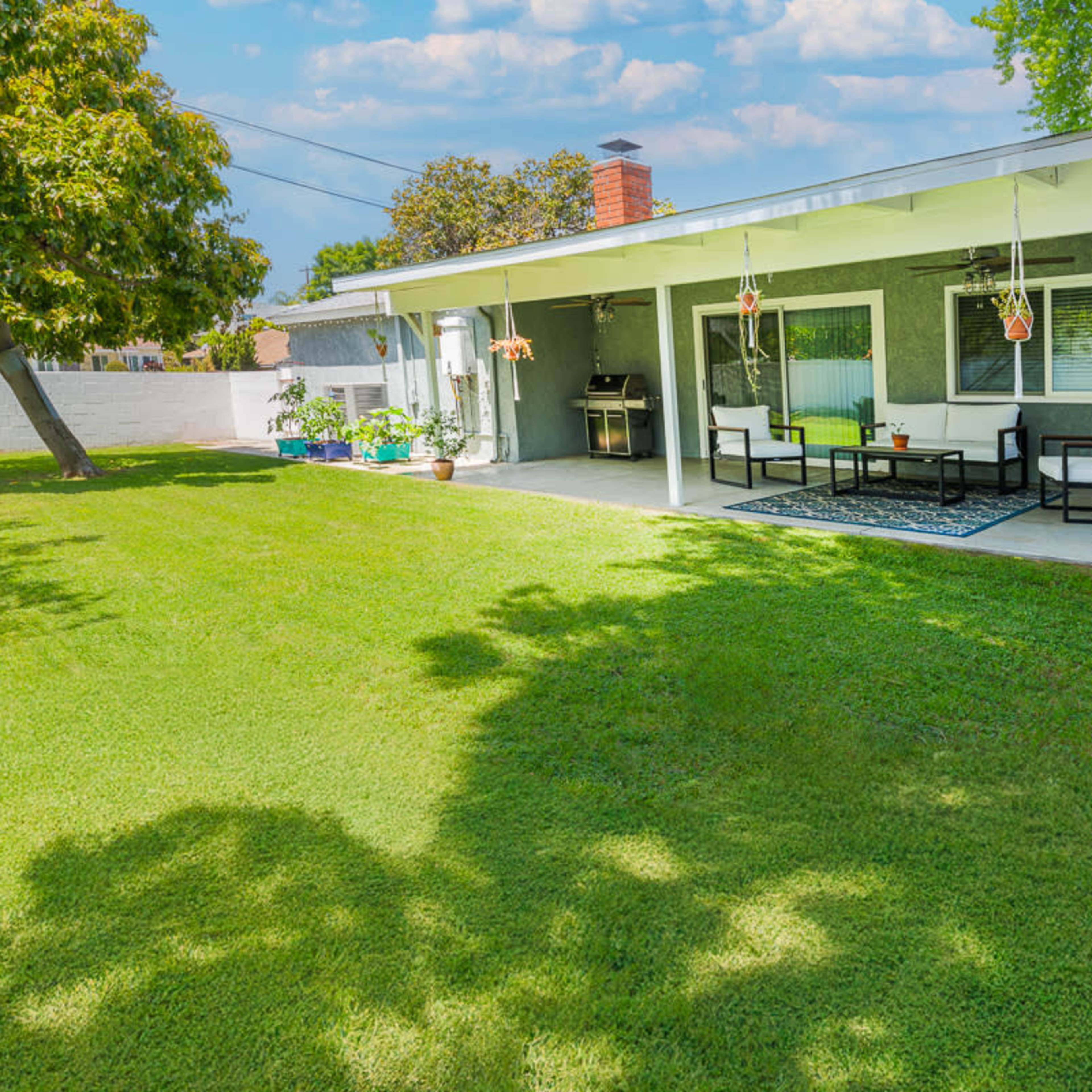 A well-maintained backyard features a patio with seating and a lawn surrounded by trees and plants.