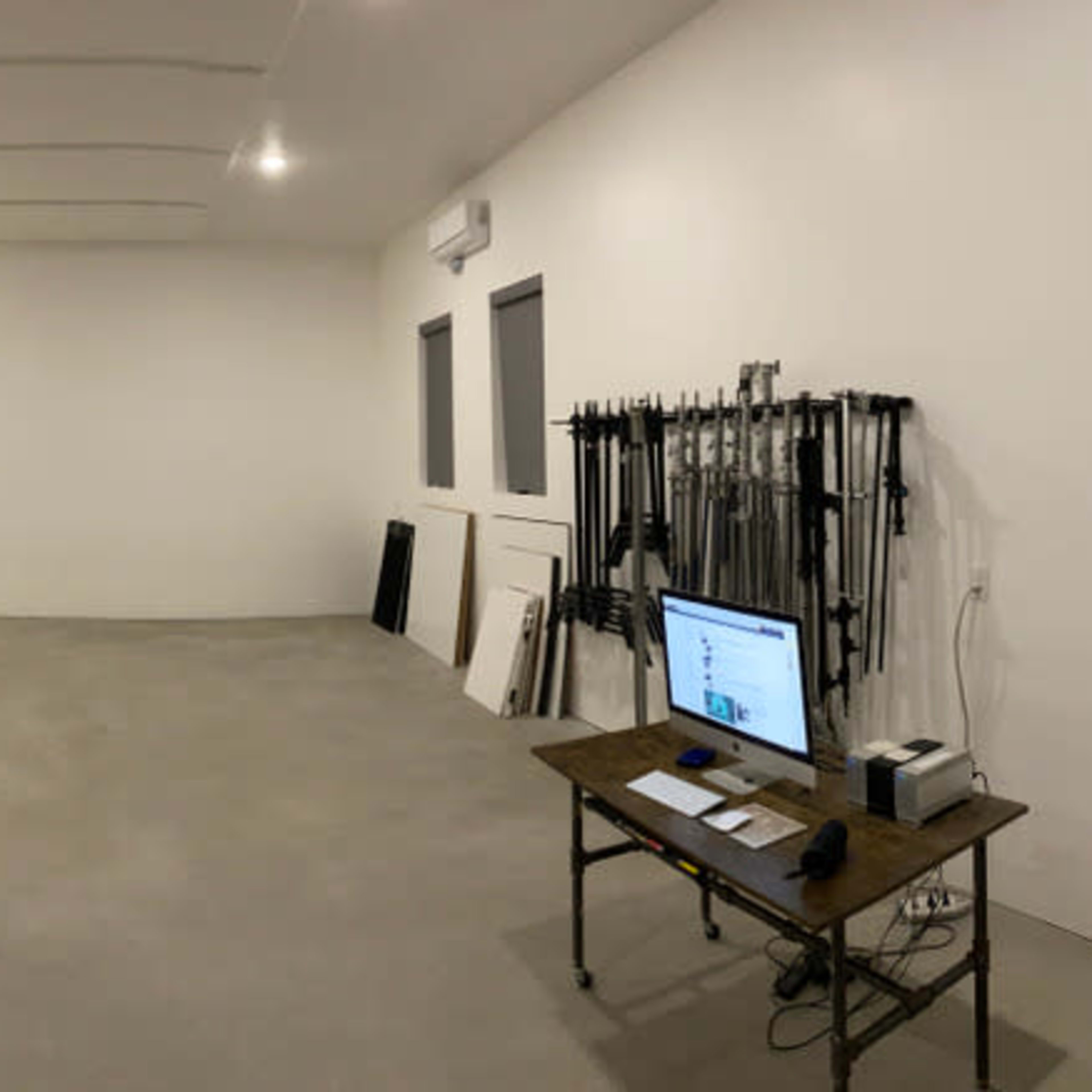 A spacious, empty room with a gray concrete floor, a black safe, a blue kitchenette, a brown couch, and a workstation with a computer on a wooden table.