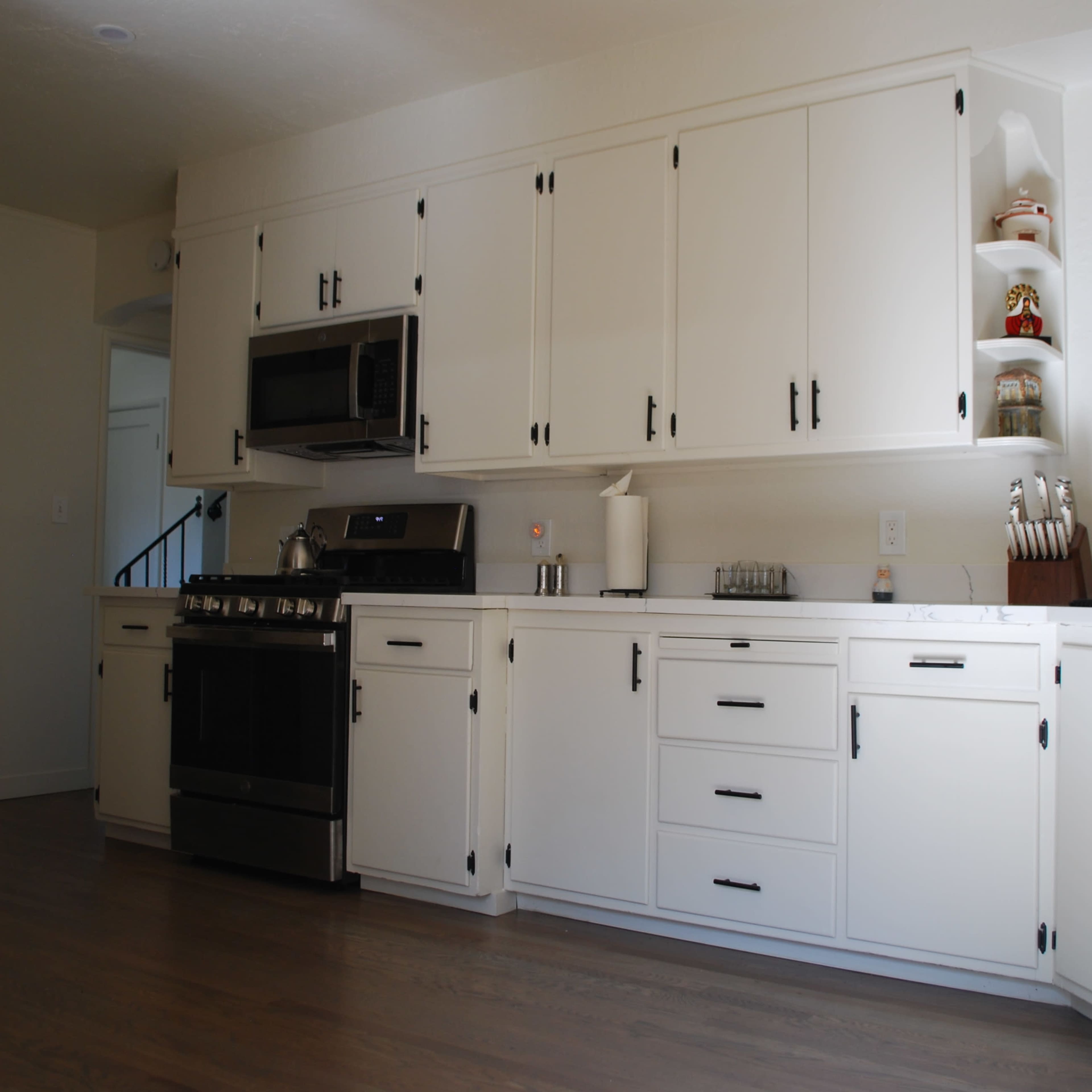 A modern kitchen with white cabinetry, stainless steel appliances, and wood flooring.