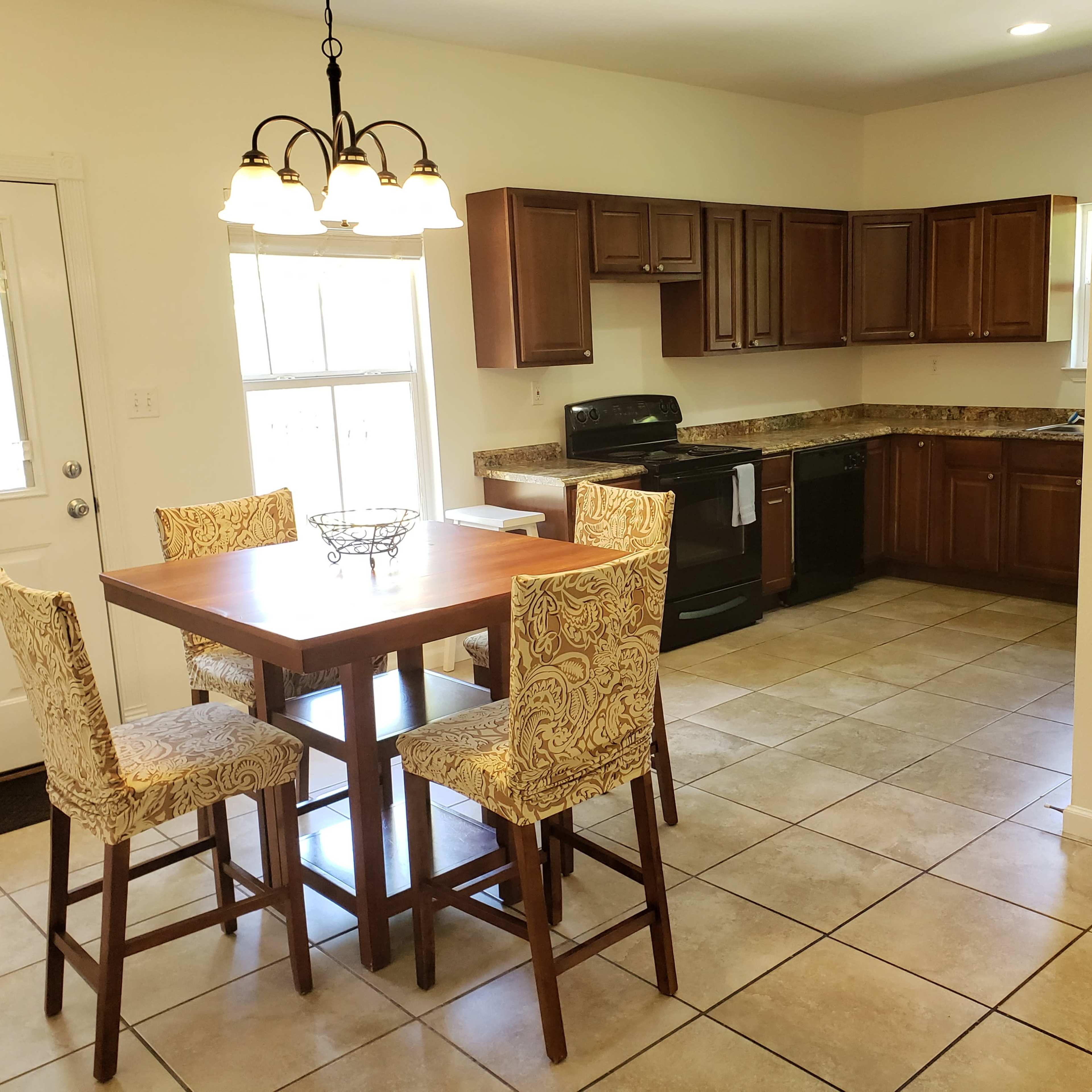 A kitchen with dark wooden cabinets, a black stove, and a table surrounded by four chairs, positioned on a tiled floor.