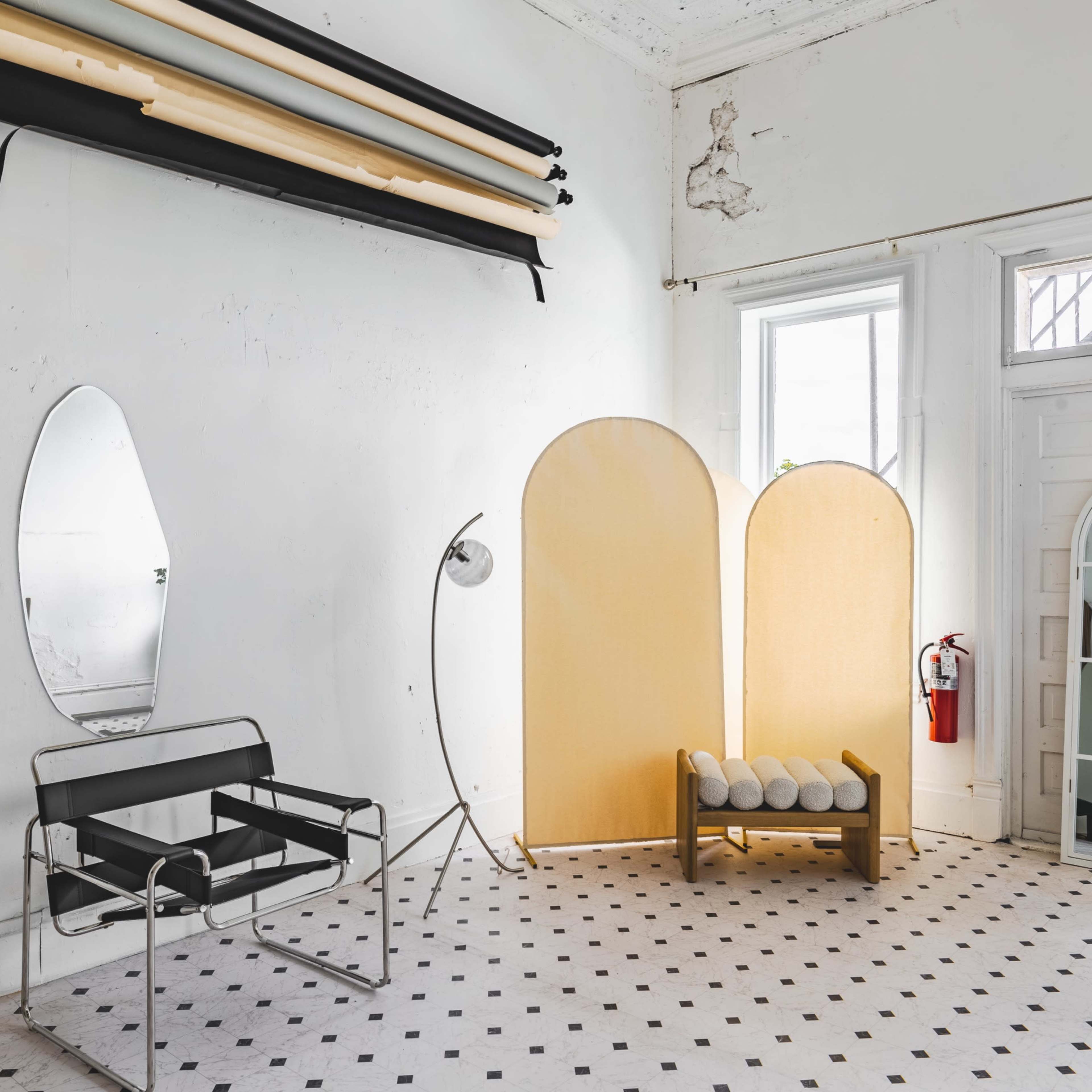 An interior space featuring a chair, backlit screens, a mirror, a lamp, and a decorative arch-shaped mirror against a patterned floor.