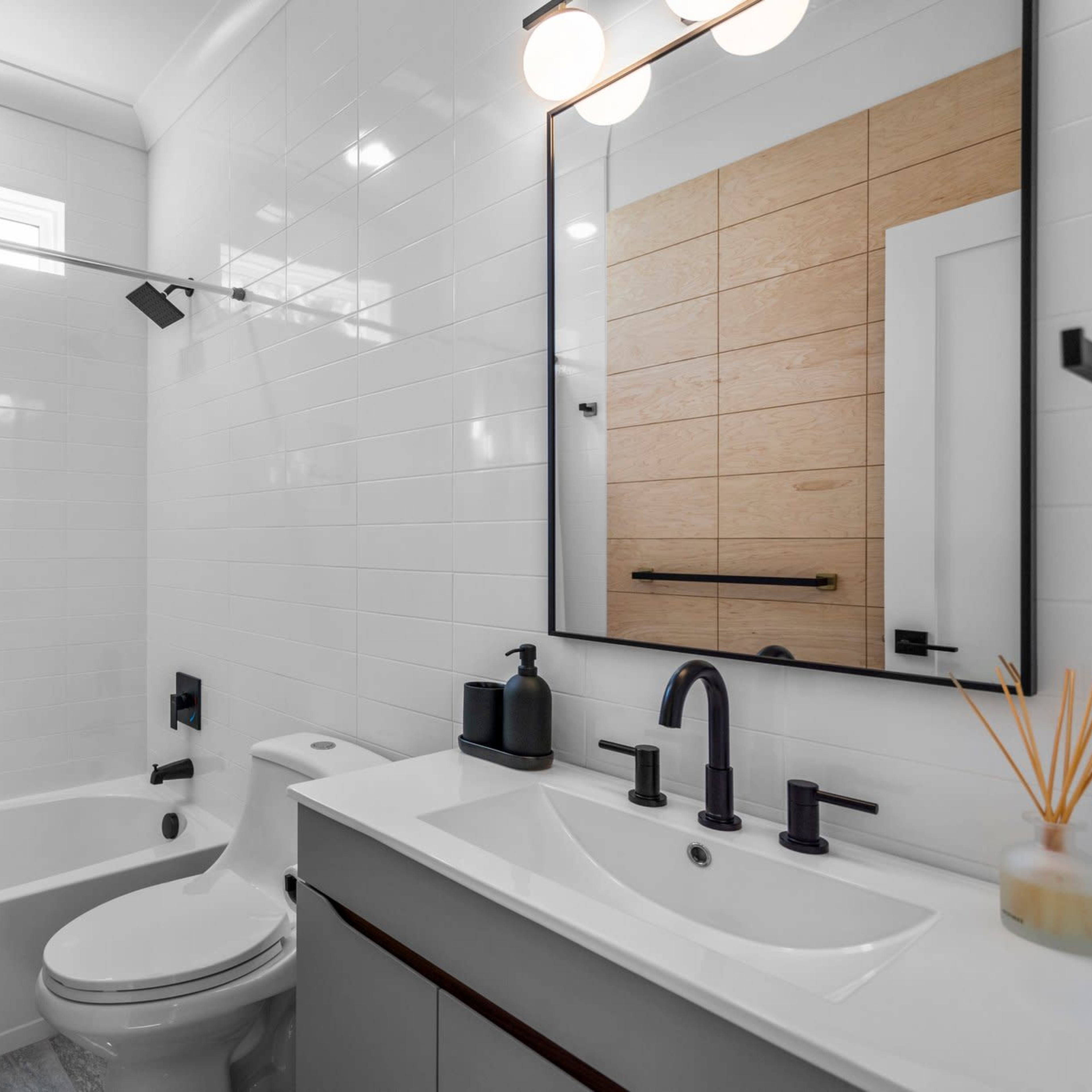 A modern bathroom featuring a tub with a shower curtain, a wall-mounted mirror, a sink with dual faucets, and a minimalist design.