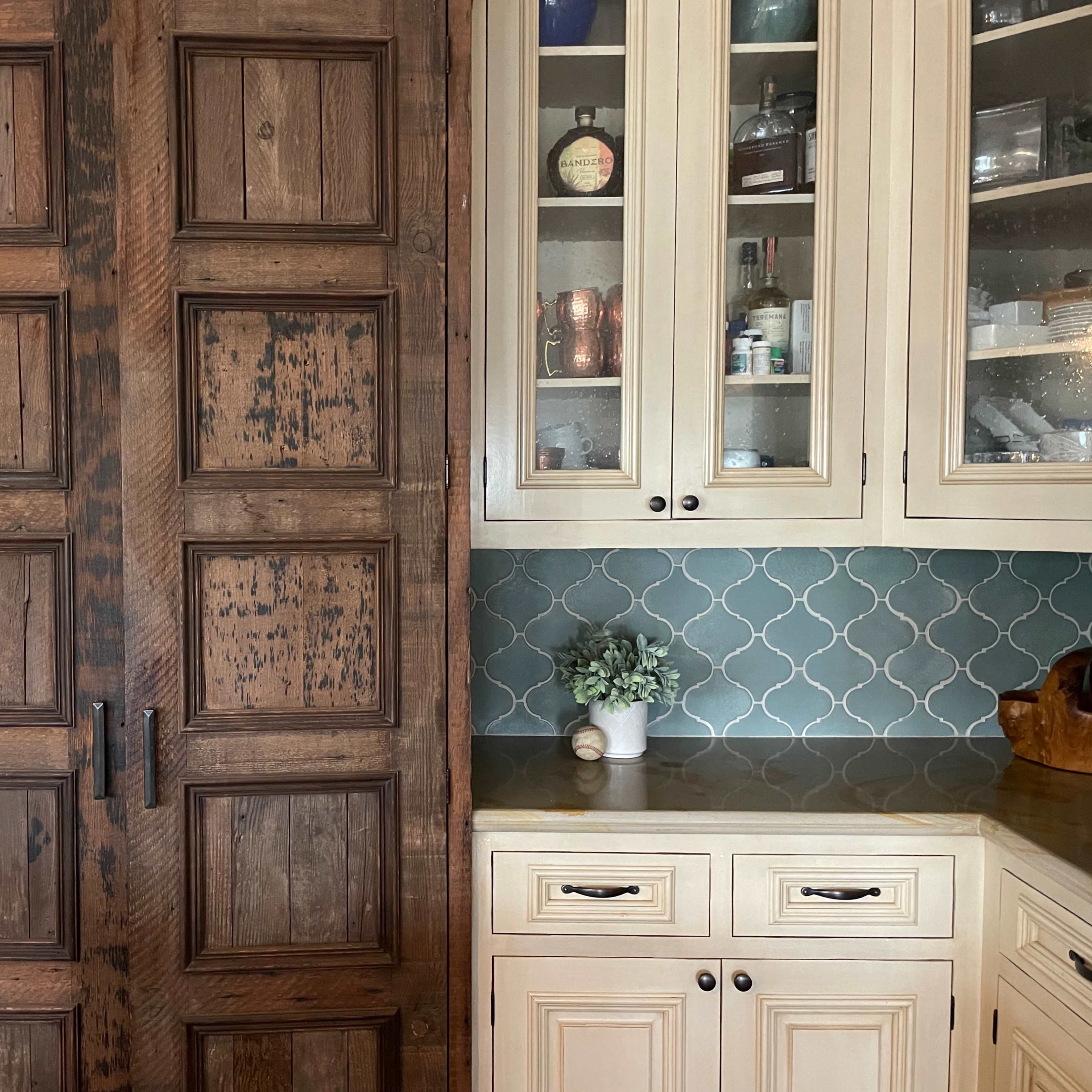 A wooden sliding door beside a set of glass-front cabinets with a teal tiled backsplash.