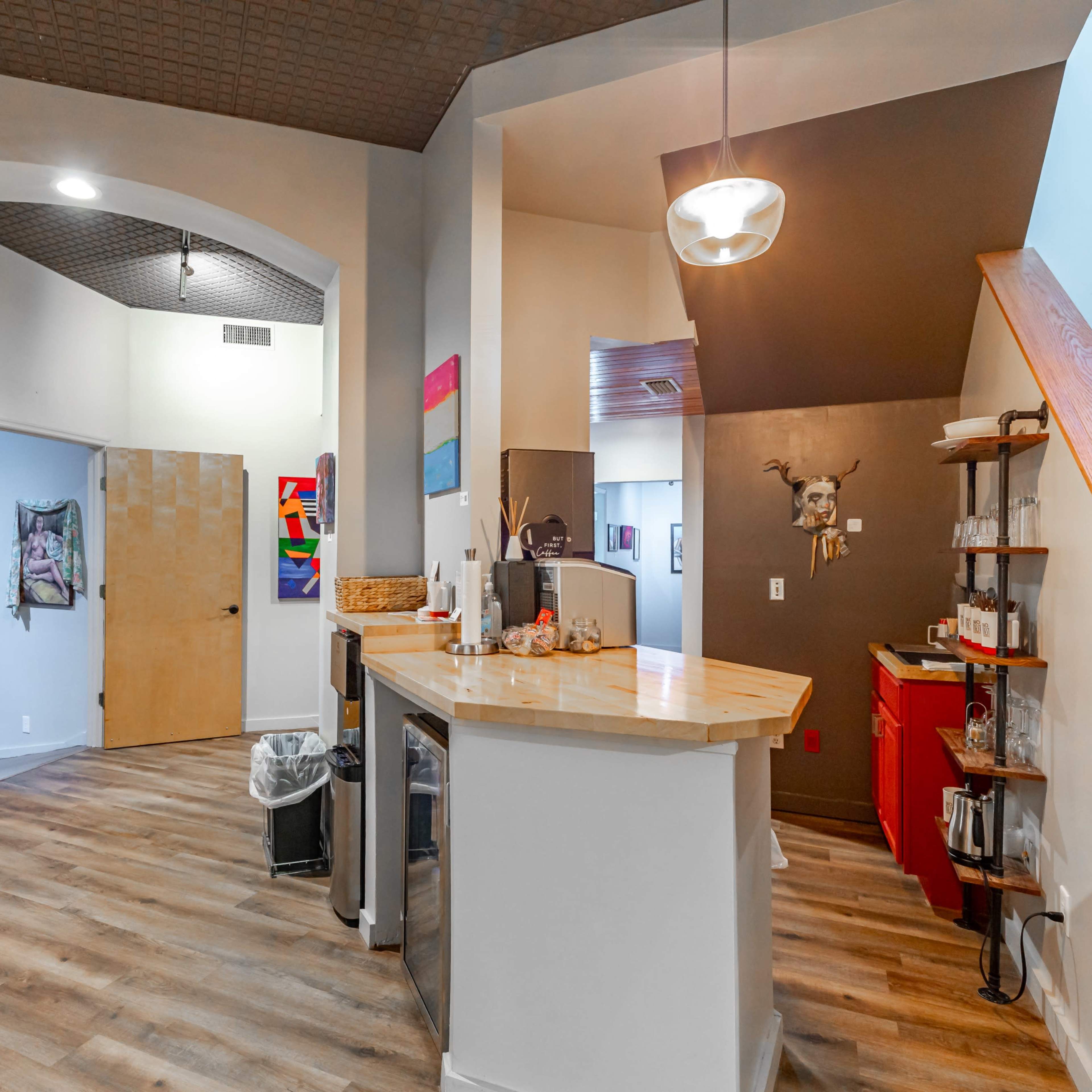 An open area featuring a kitchen bar with seating, leading to a hallway and staircase, with art pieces displayed on the walls.